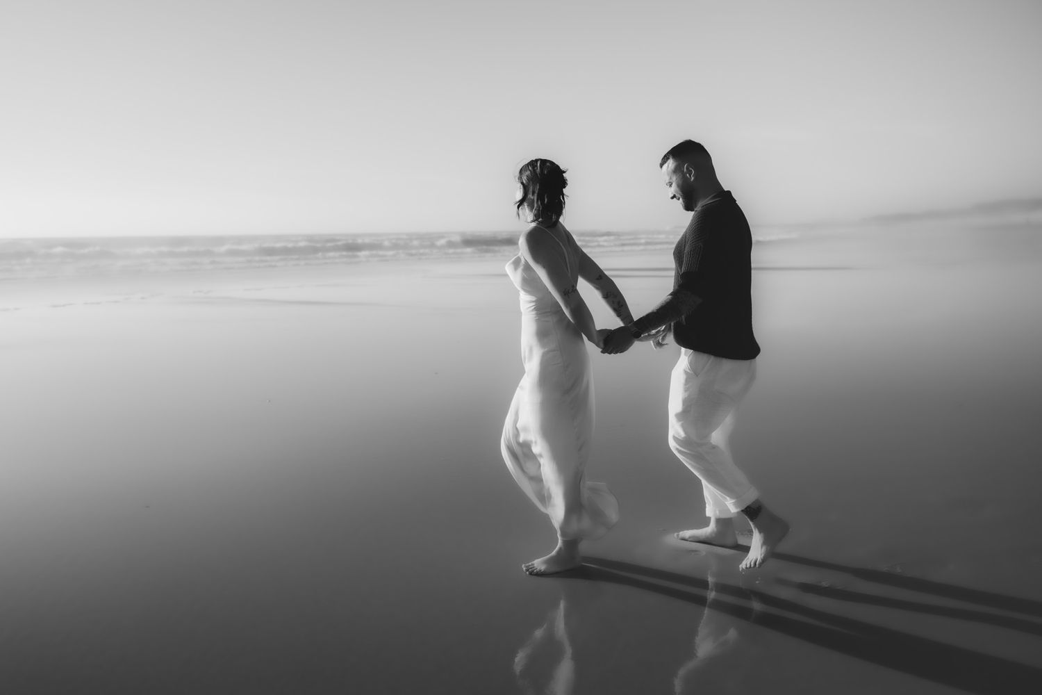 Black and white silhouette of two people walking along a misty beach.