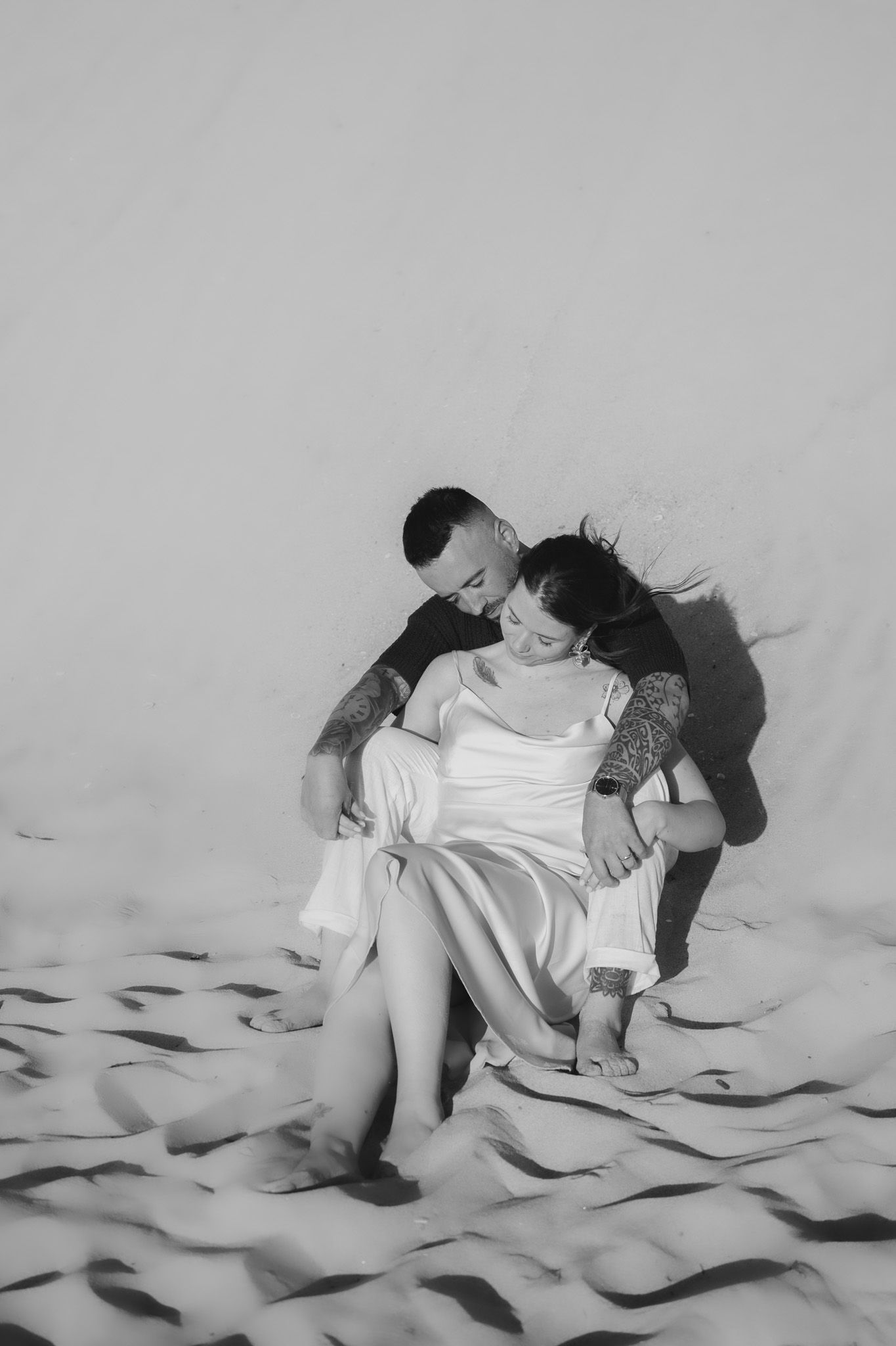 A couple lying on white sheets in artistic black and white photography sequence.