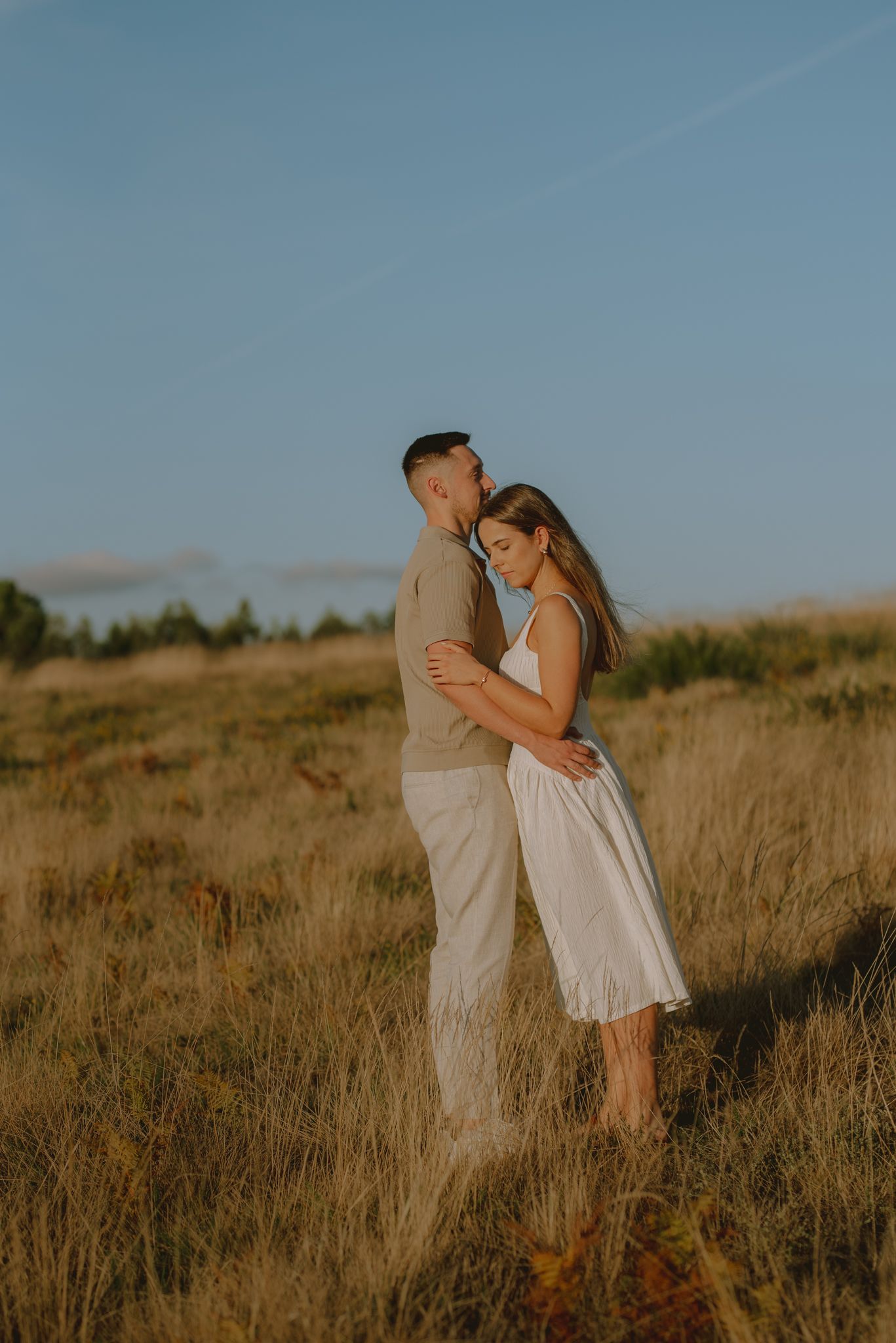 A romantic couple embraces in a golden field during sunset creating a dreamy silhouette.