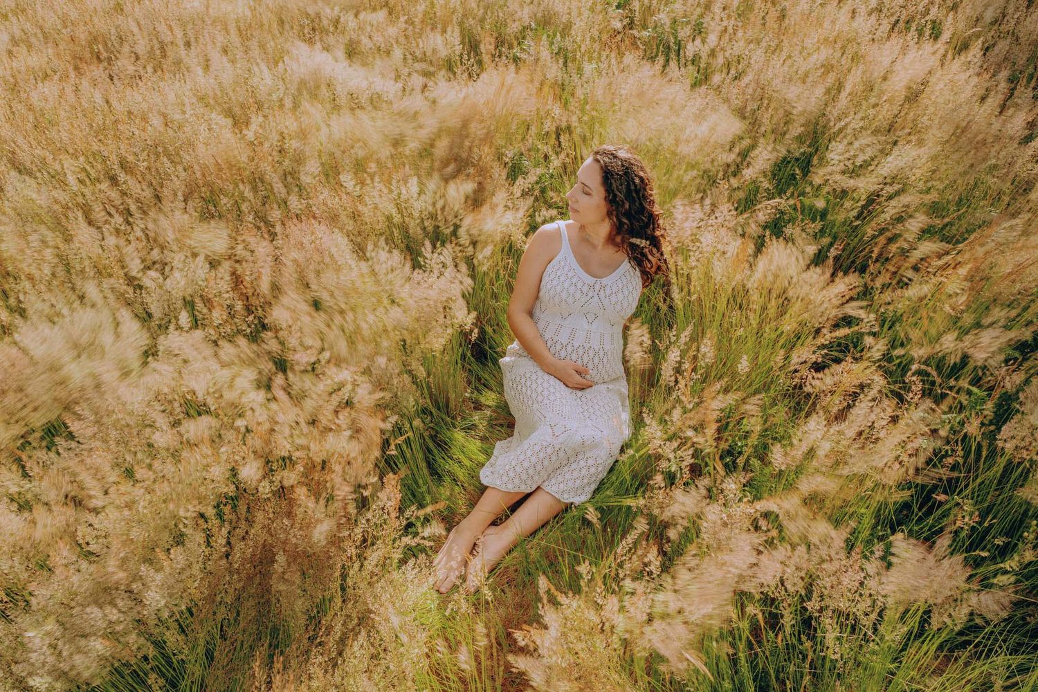 A woman in a white dress poses gracefully in a sun-drenched field of golden wheat during golden hour.