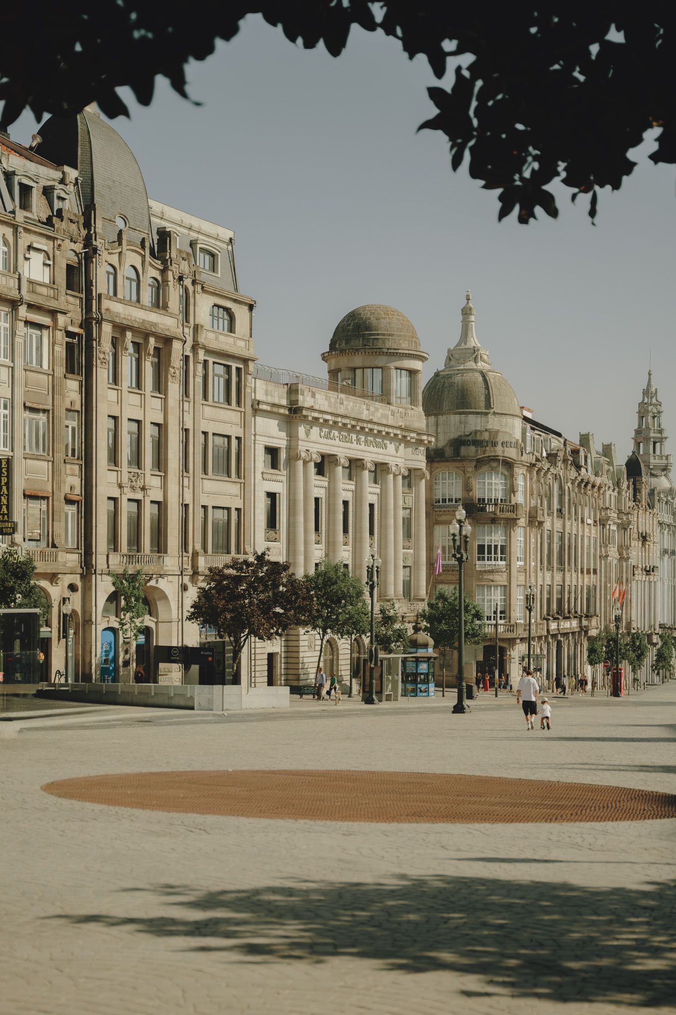Grand European-style architecture with domed buildings and ornate facades lines a spacious plaza under a cloudy sky.