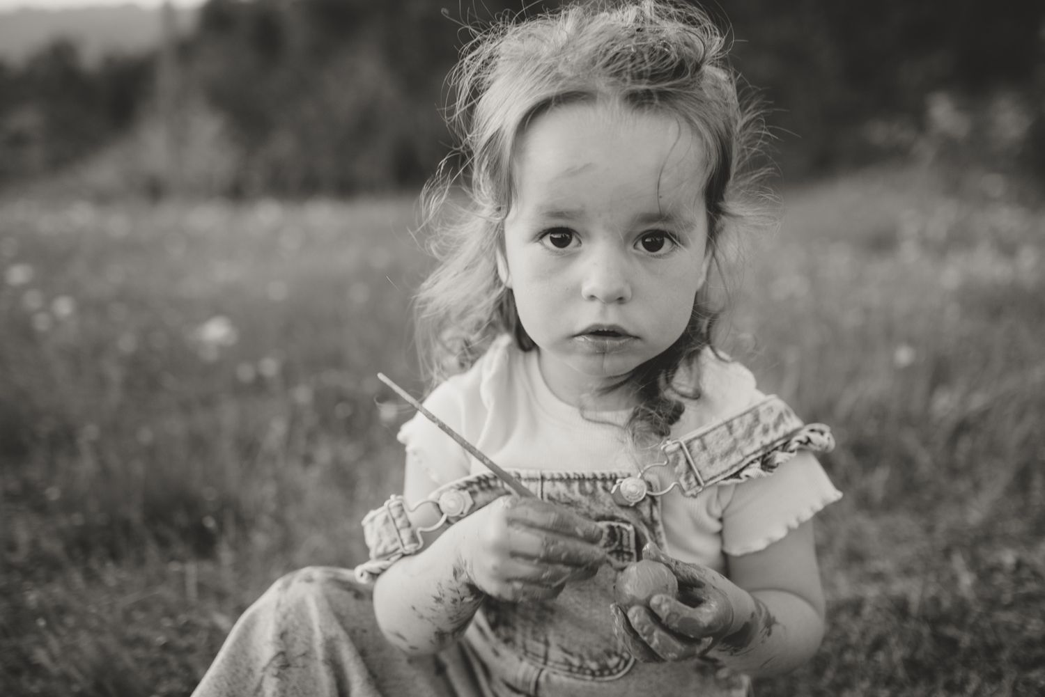 Black and white portrait of a child sitting in a grassy meadow.
