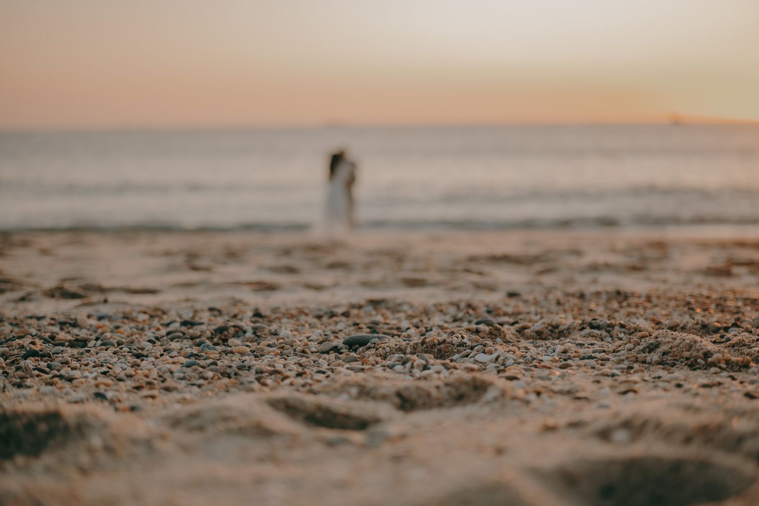 Close-up of textured beach sand with blurred horizon at sunset.