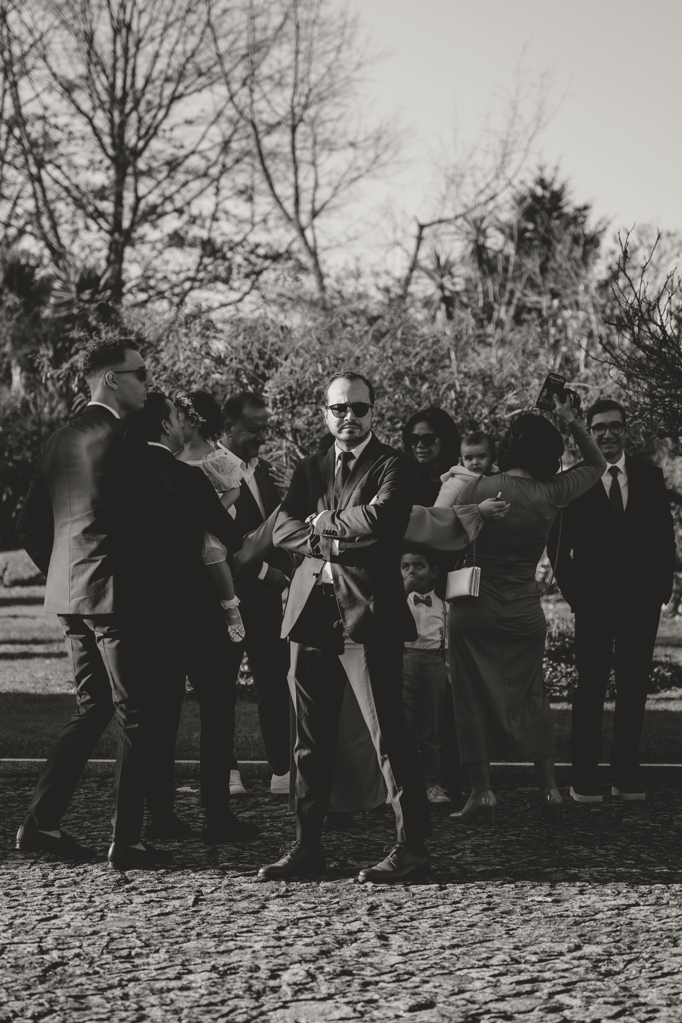 A group of formally dressed guests stand together on a stone walkway during an outdoor event.