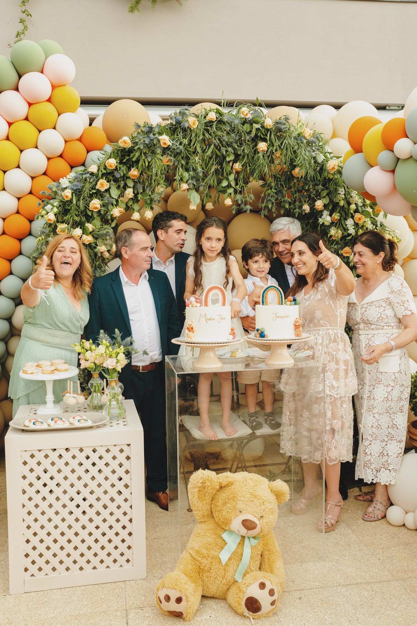 A celebration scene with pastel balloon decor, dessert tables, and a large teddy bear.