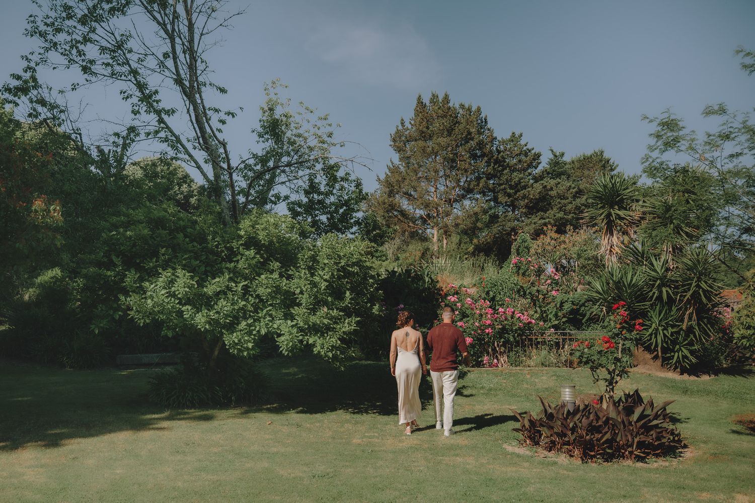 Couple walking together in distance through lush garden landscape on sunny day.