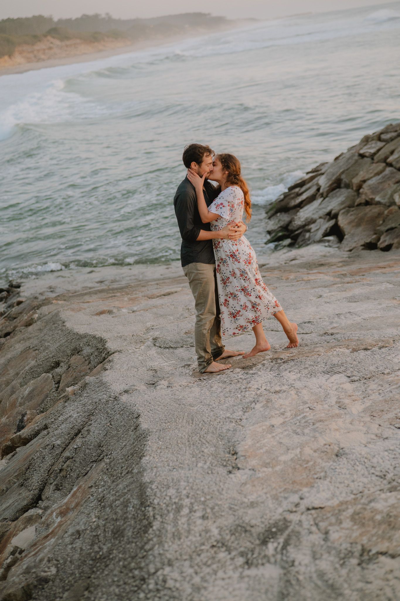 Couple sharing an intimate moment on rocky coastal cliffs at sunset.