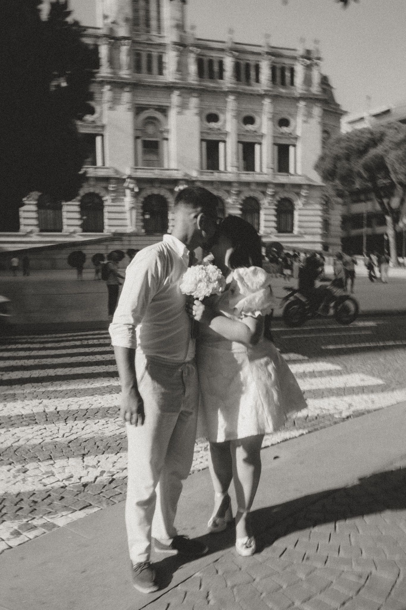 People walking on a cobblestone path near a grand historic building in black and white.