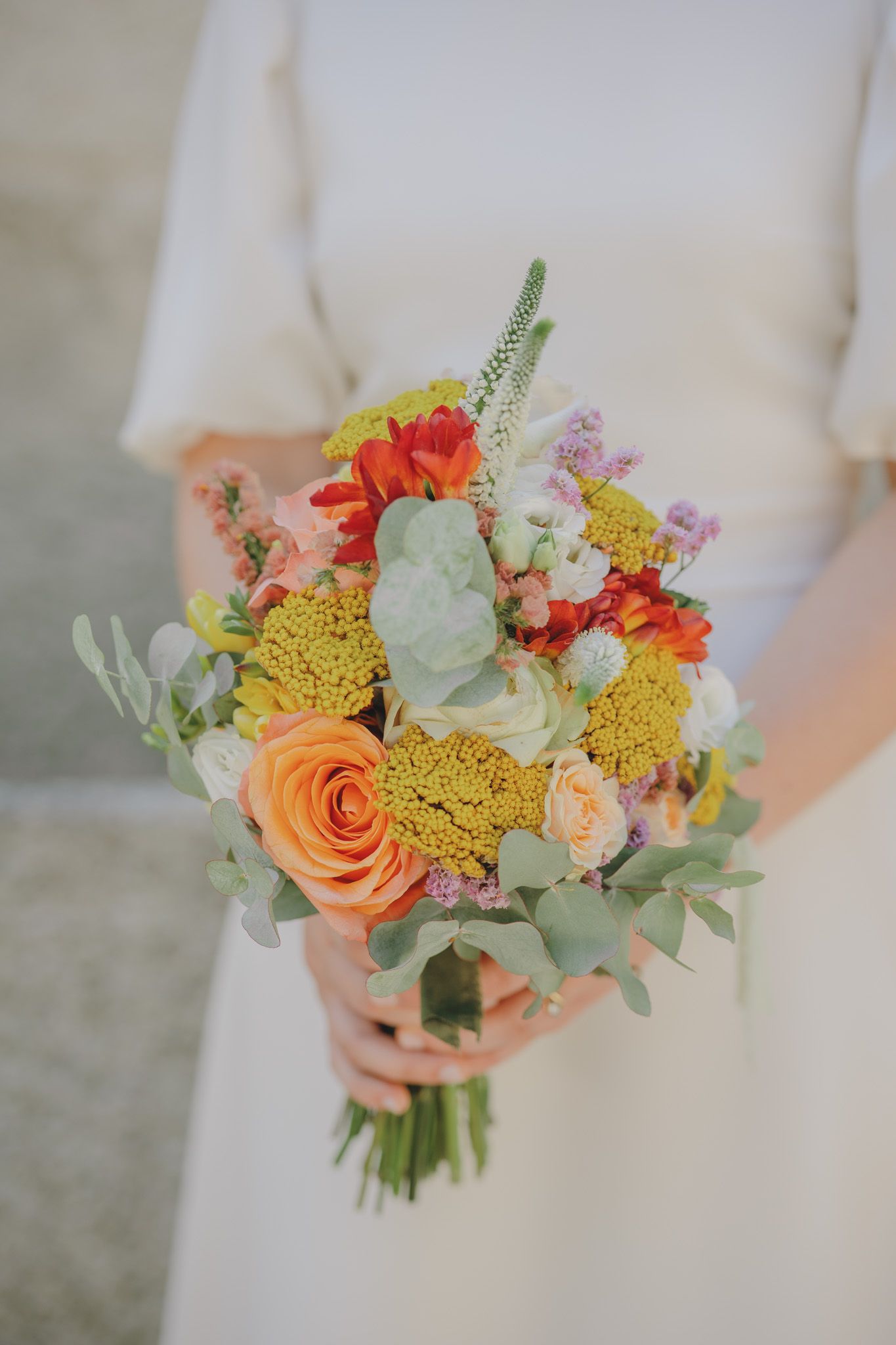 Colorful wedding bouquet with orange roses, yellow flowers and greenery.