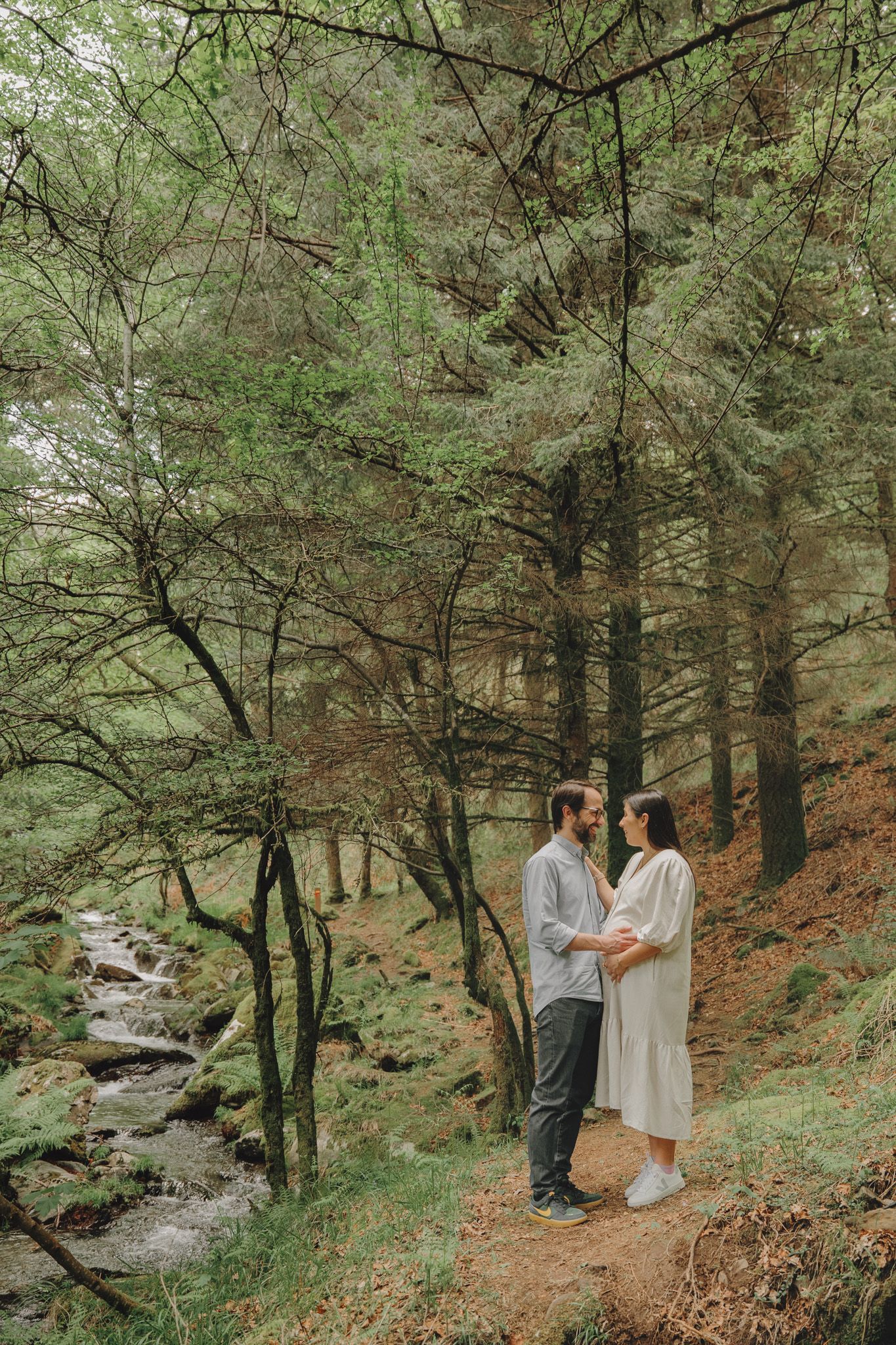 Romantic forest scene with couple standing near a flowing stream among pine trees.
