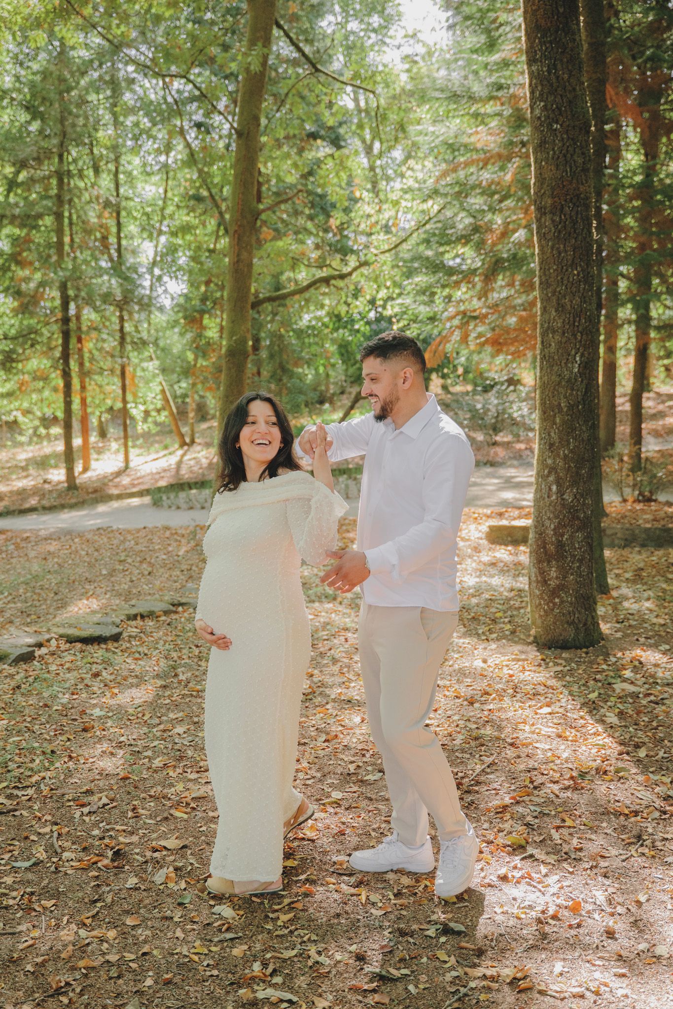 Couple in white outfits share intimate moment in wooded setting.
