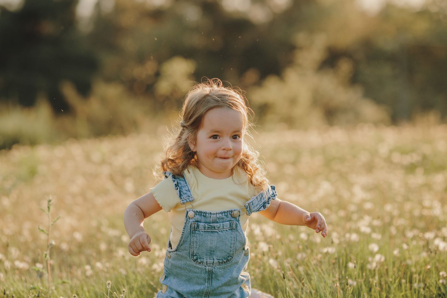 Carefree running through a field of wildflowers at golden hour wearing blue denim overalls.