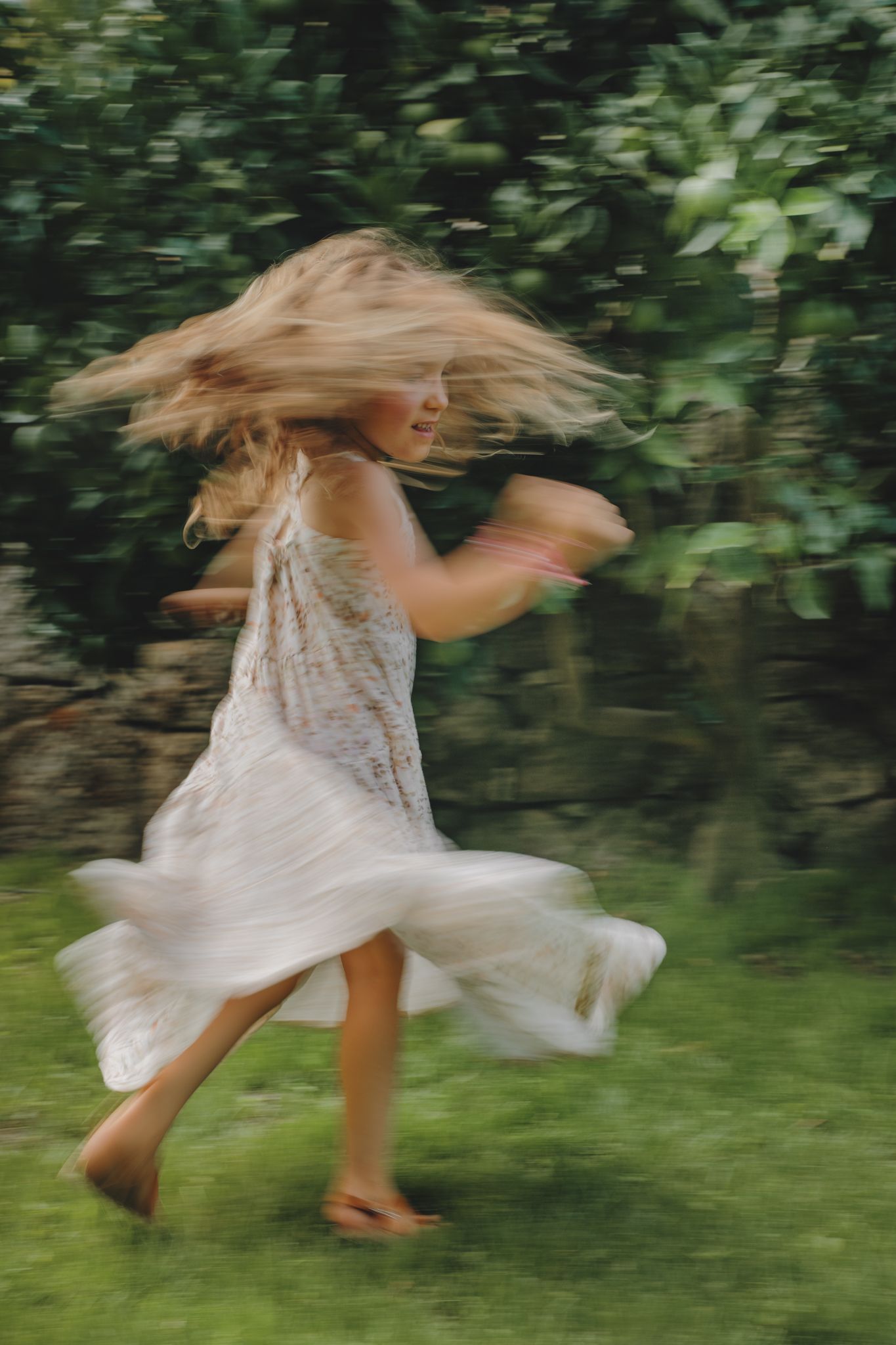 A figure in a flowing white dress spins and twirls through a garden setting creating a dreamy motion blur effect.