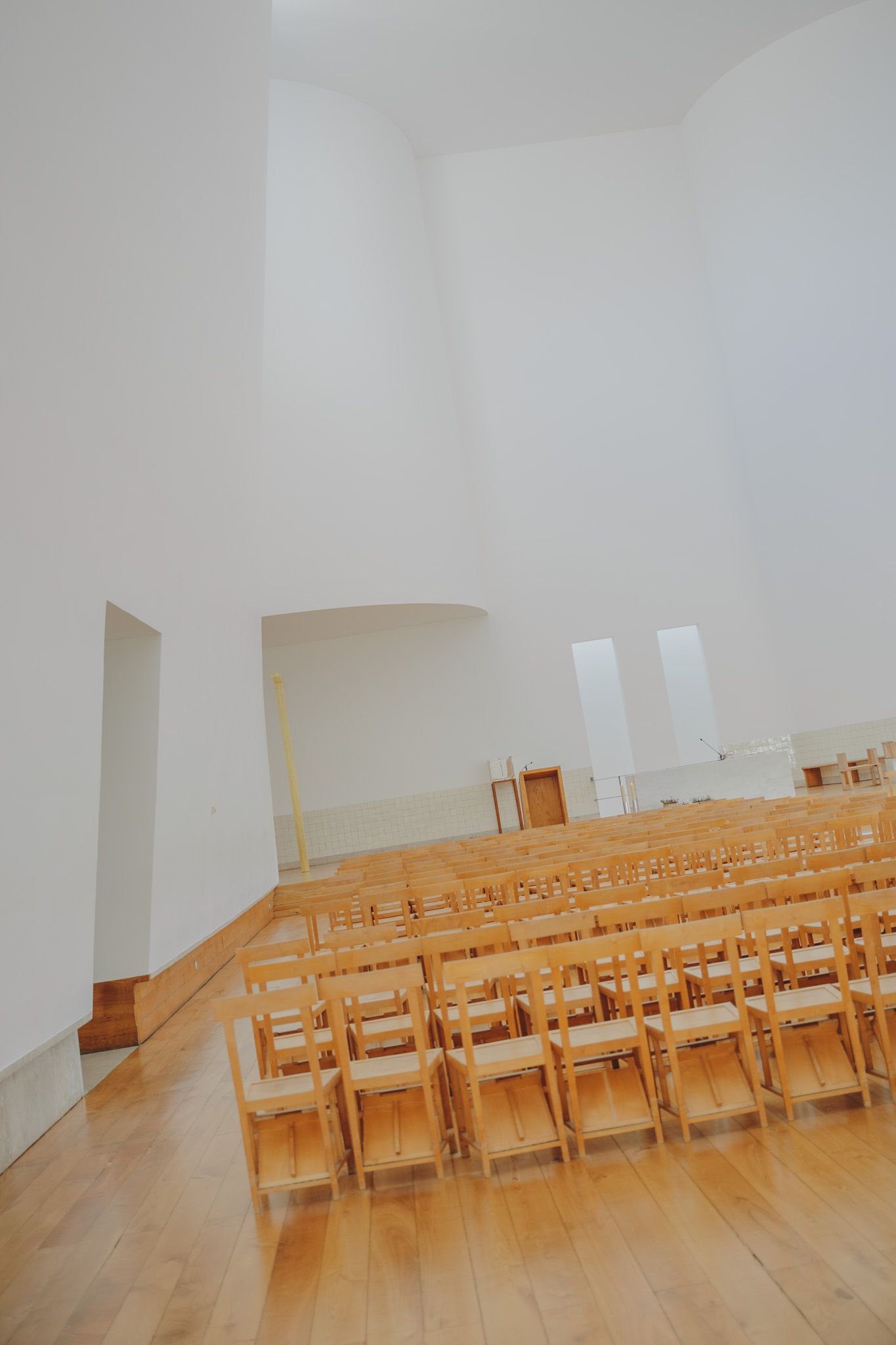 Rows of wooden folding chairs set up in a bright, minimalist white church interior.