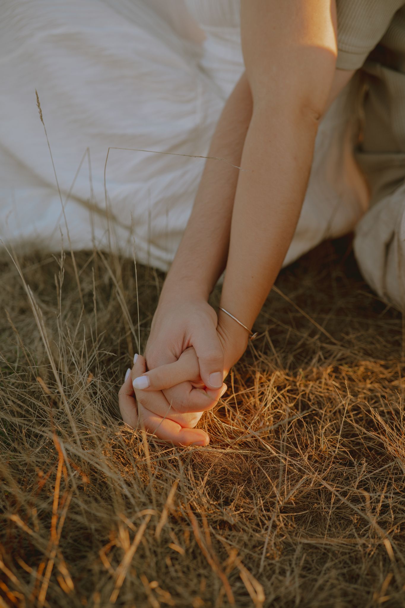 Close-up detail of hands resting on dry grass in warm evening light.