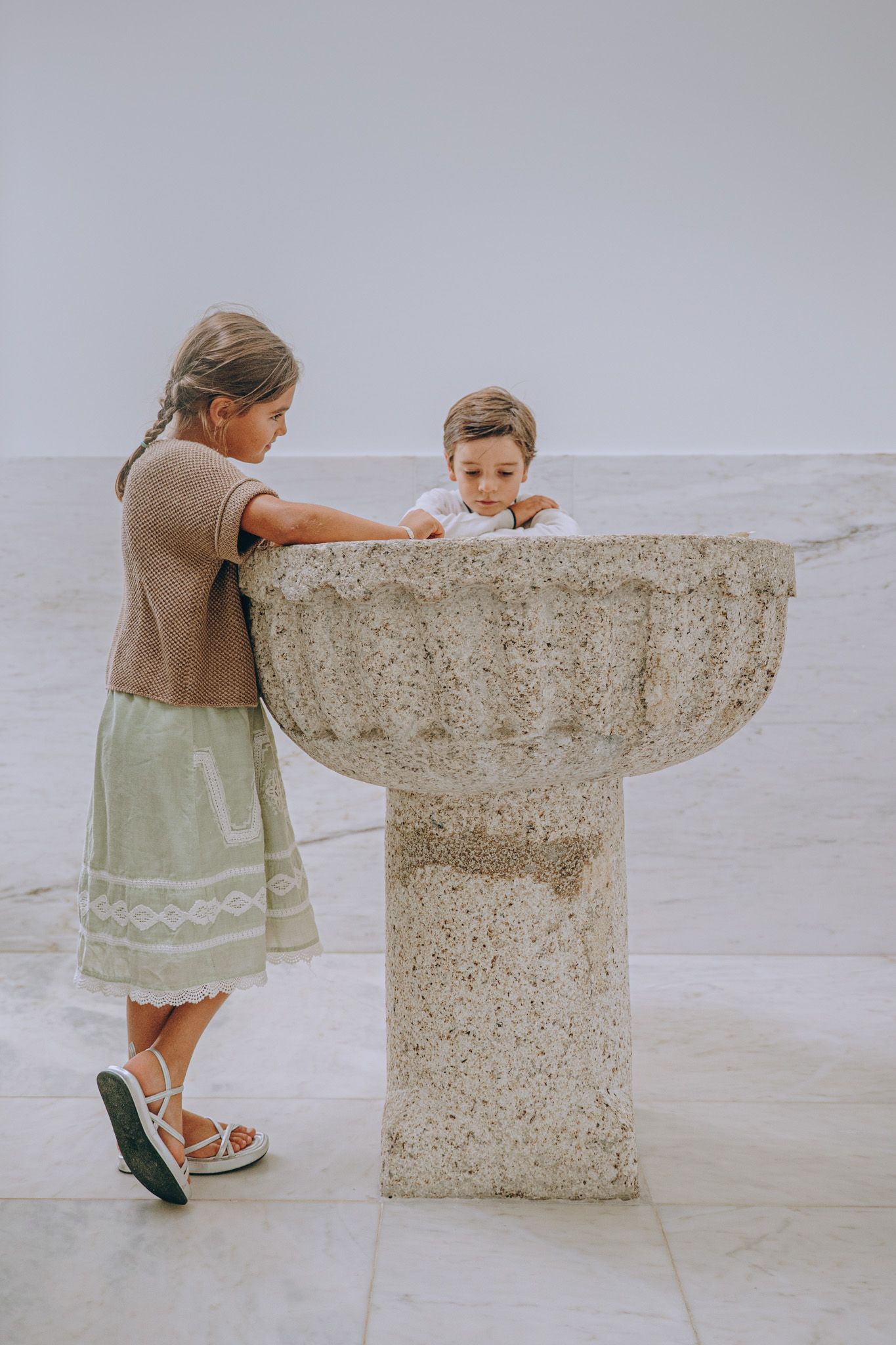 Child peering over edge of stone baptismal font in church.