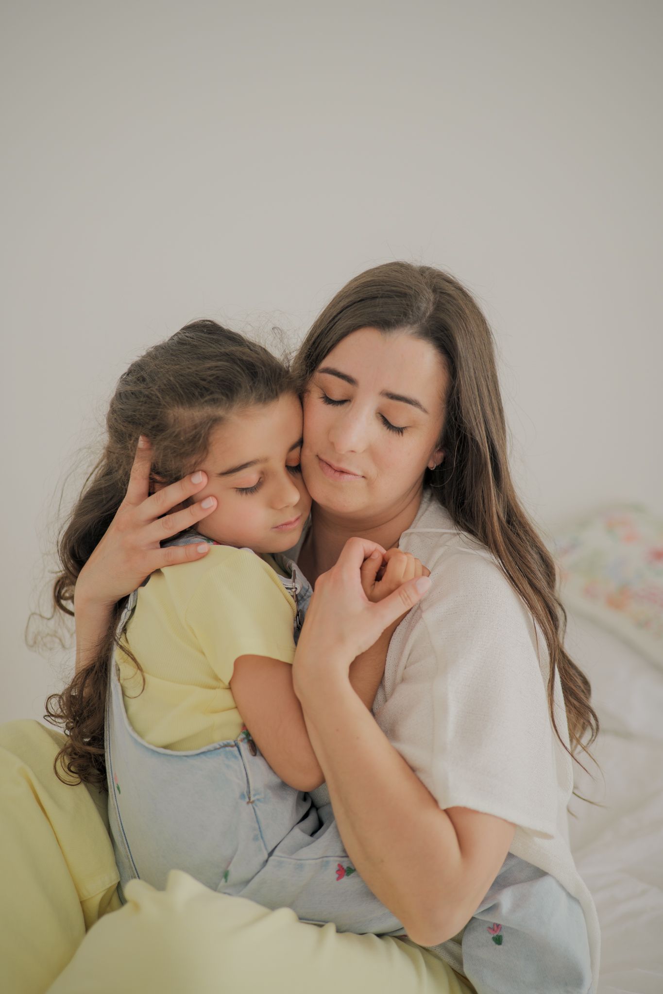 A mother tenderly embraces her young daughter, both with closed eyes, sharing a peaceful moment together.