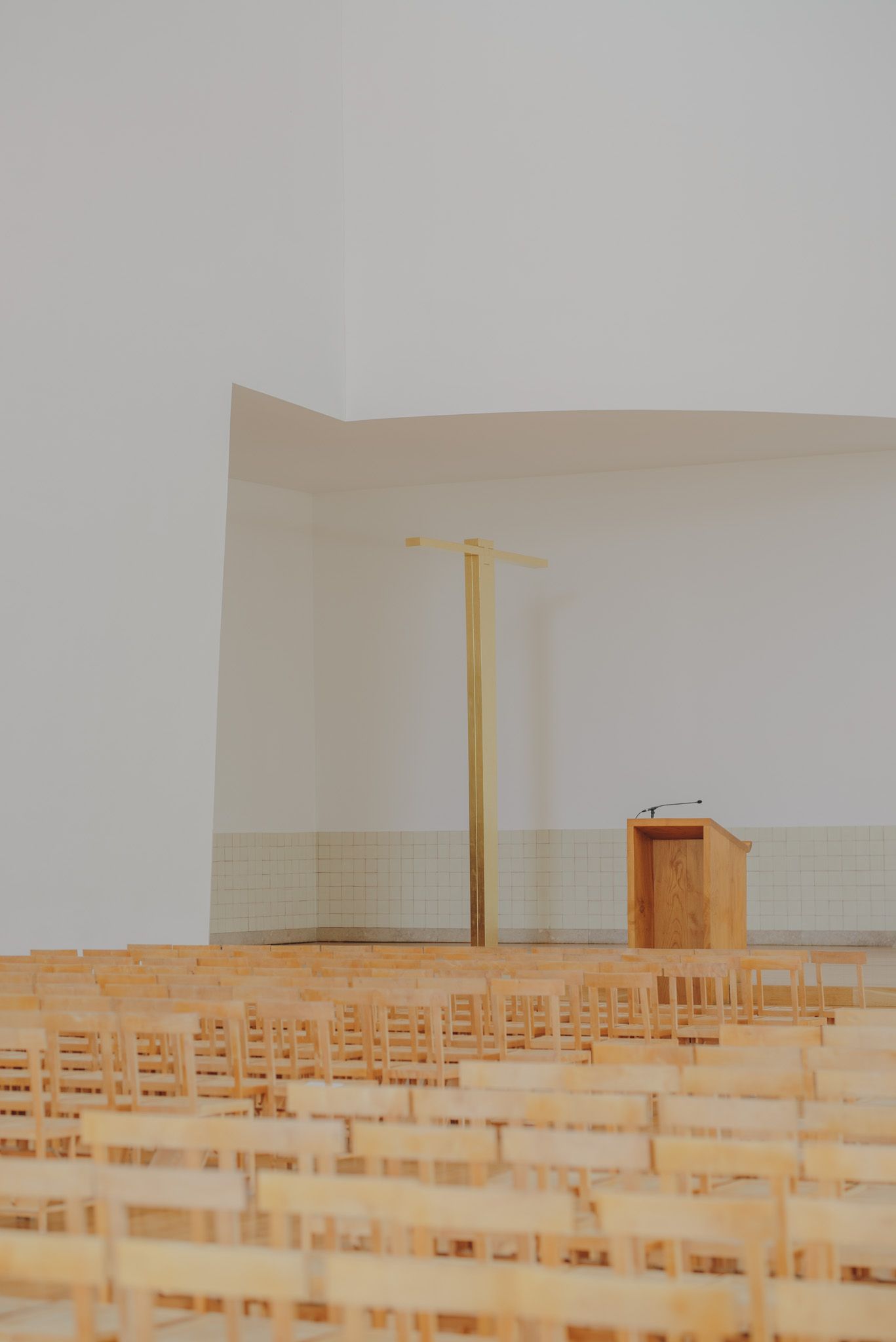 Empty wooden chairs arranged in rows inside a minimalist modern church sanctuary.