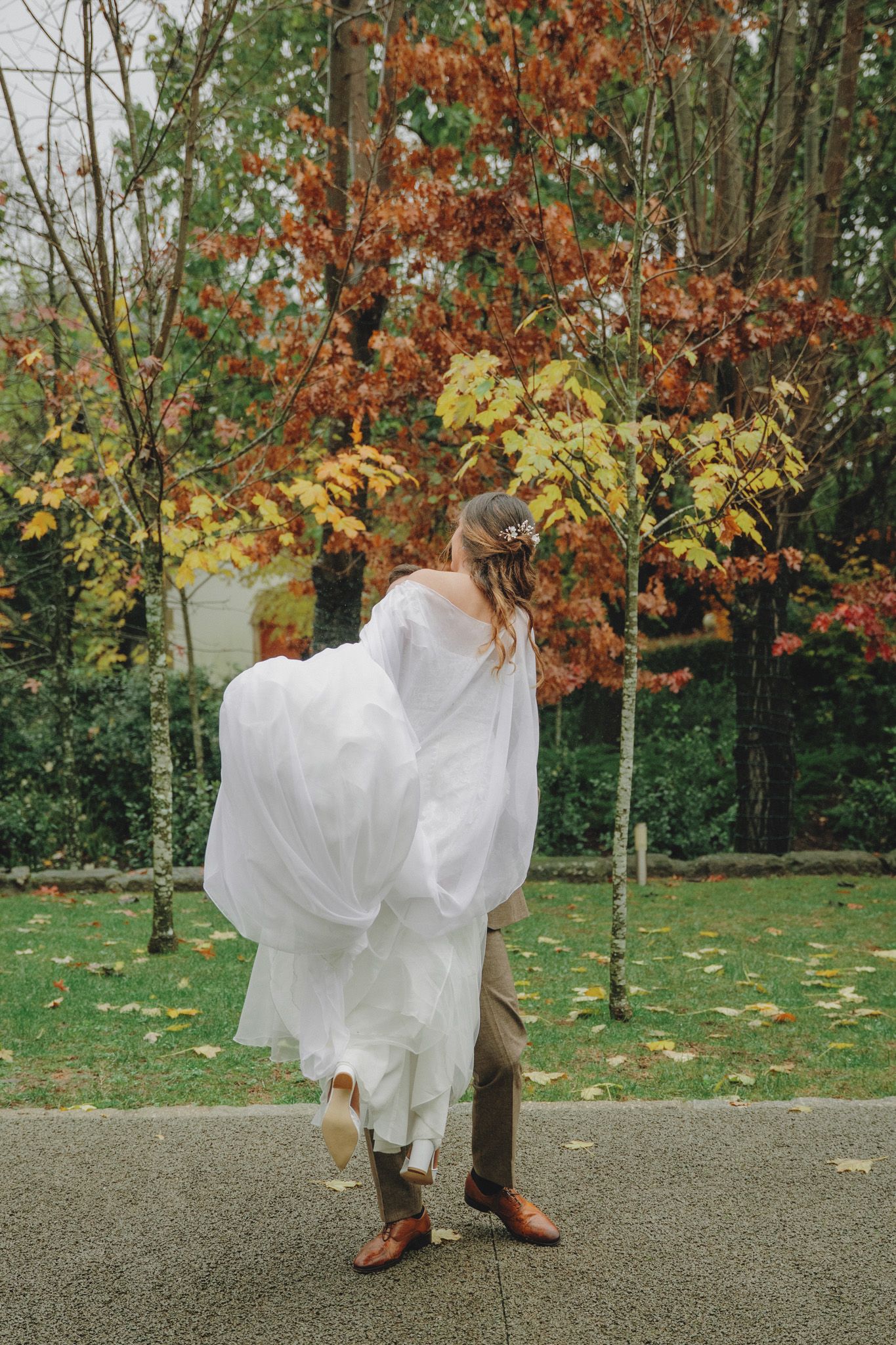 White wedding dress flowing in autumn breeze among colorful fall foliage.