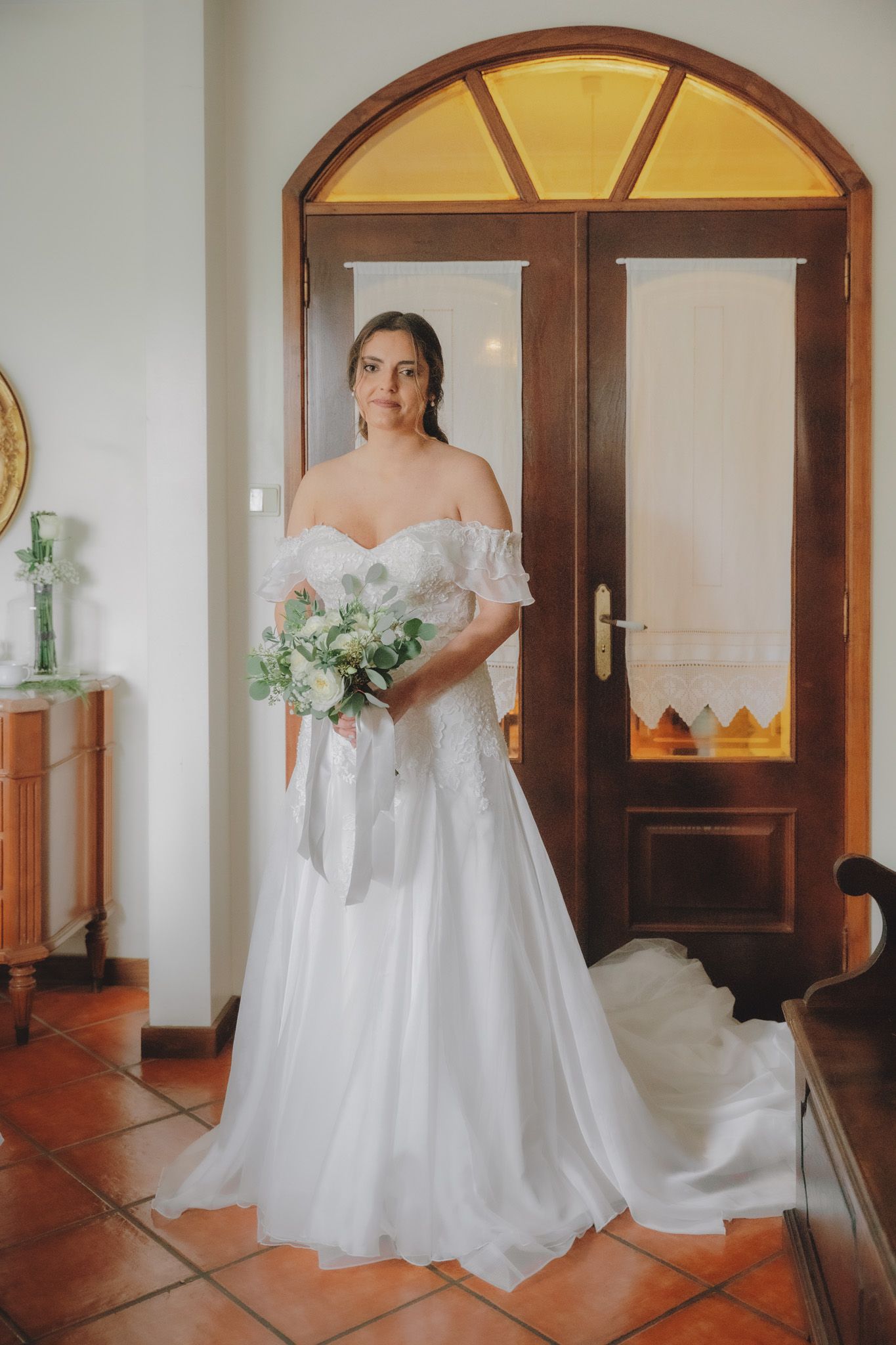 White wedding gown with off-shoulder design photographed in a room with arched doorways.
