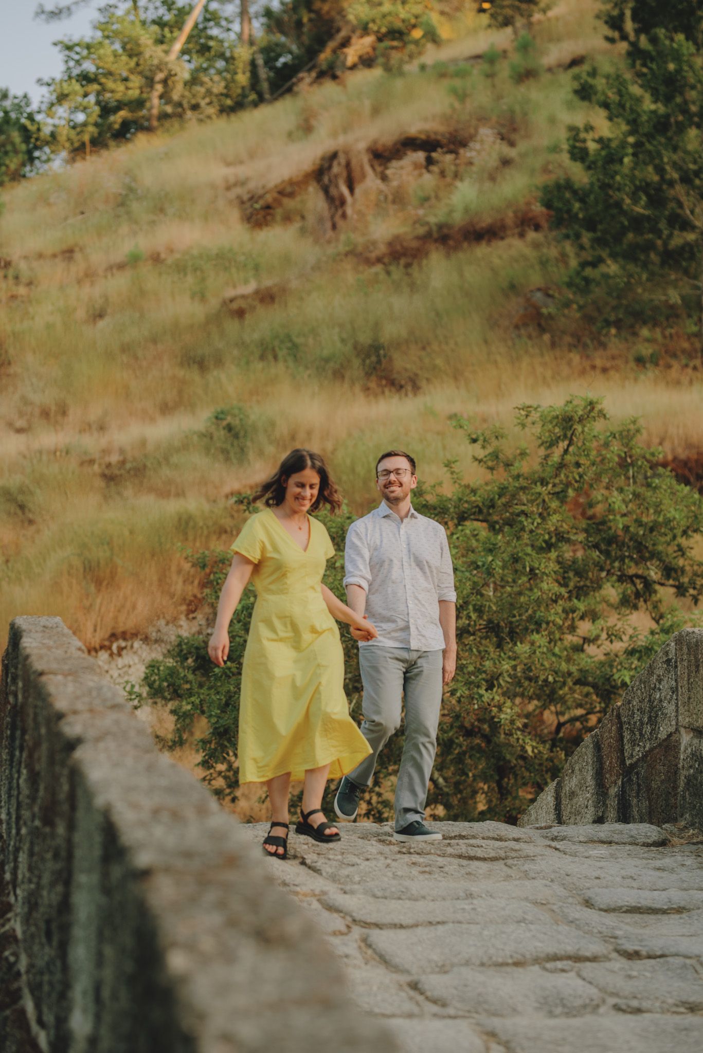A couple stands together on a rocky outcrop with yellow dress flowing in the breeze.