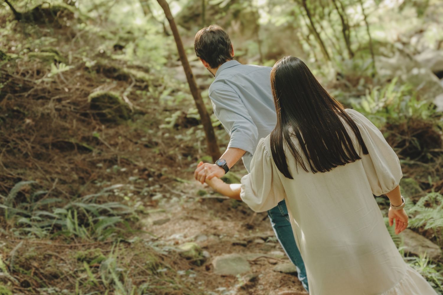 Two people walk up a steep forest trail holding hands.