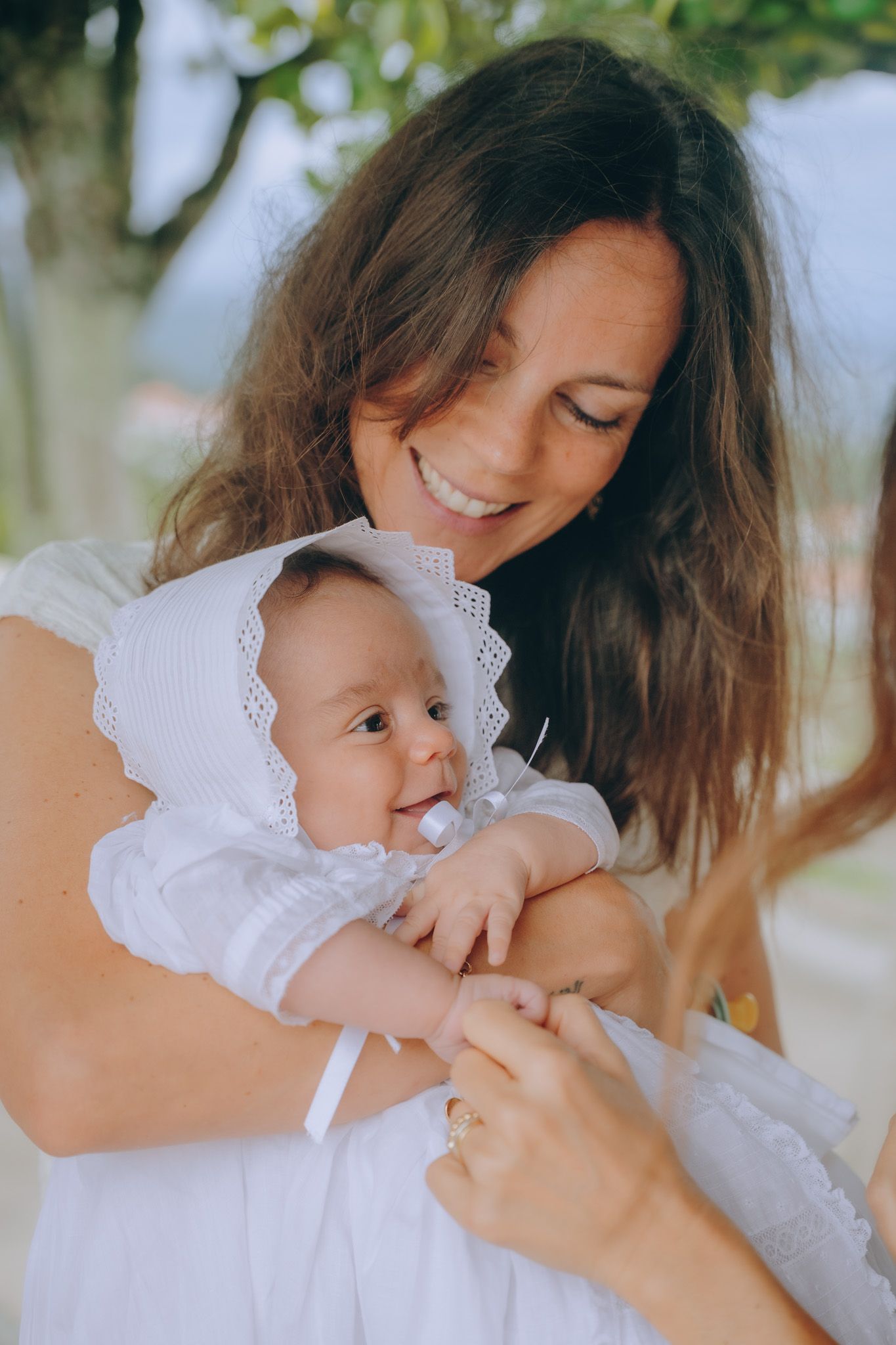 Tender moment between parent and child wearing white lace outfits outdoors.
