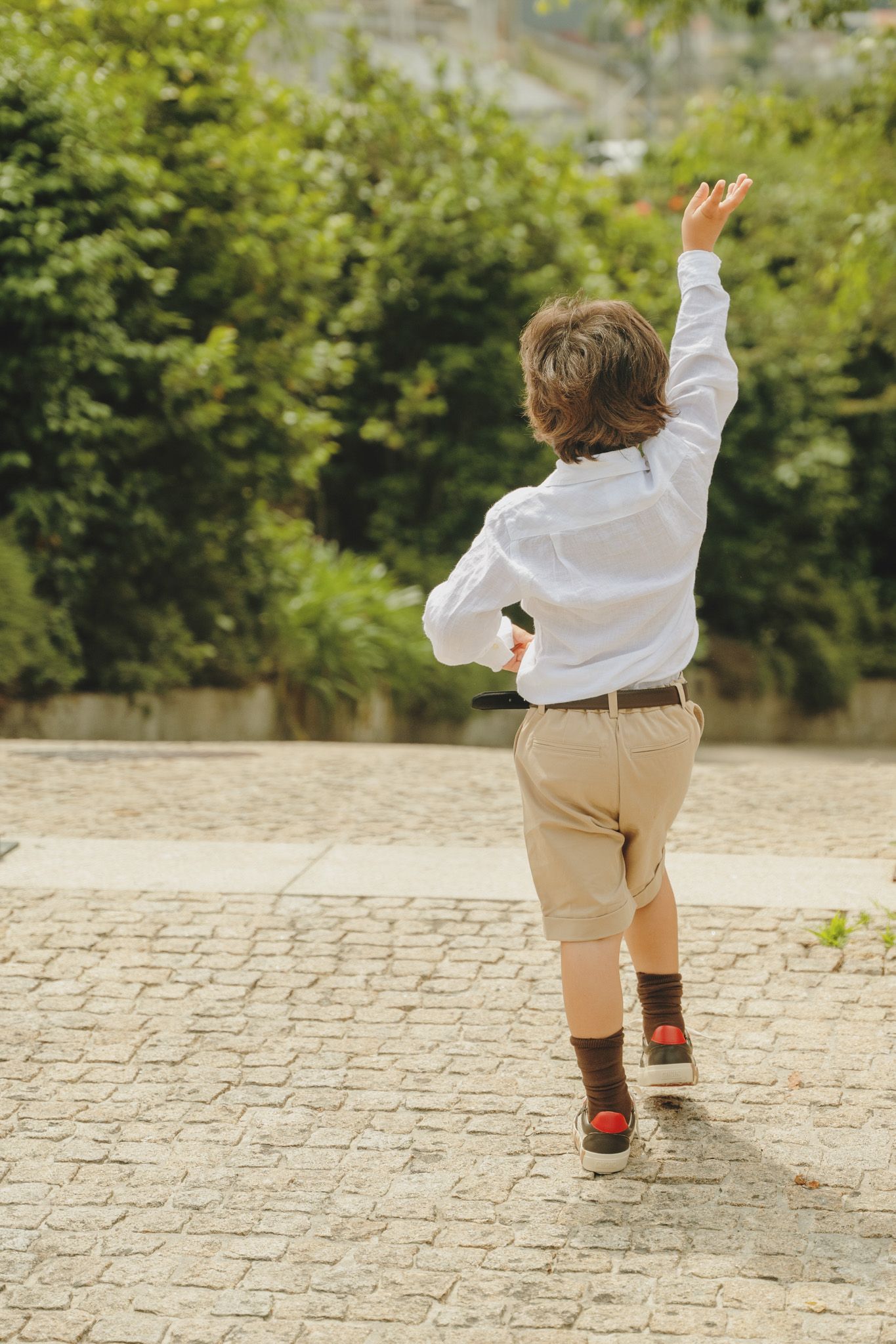 Small child in white shirt and khaki shorts running on stone pavement.