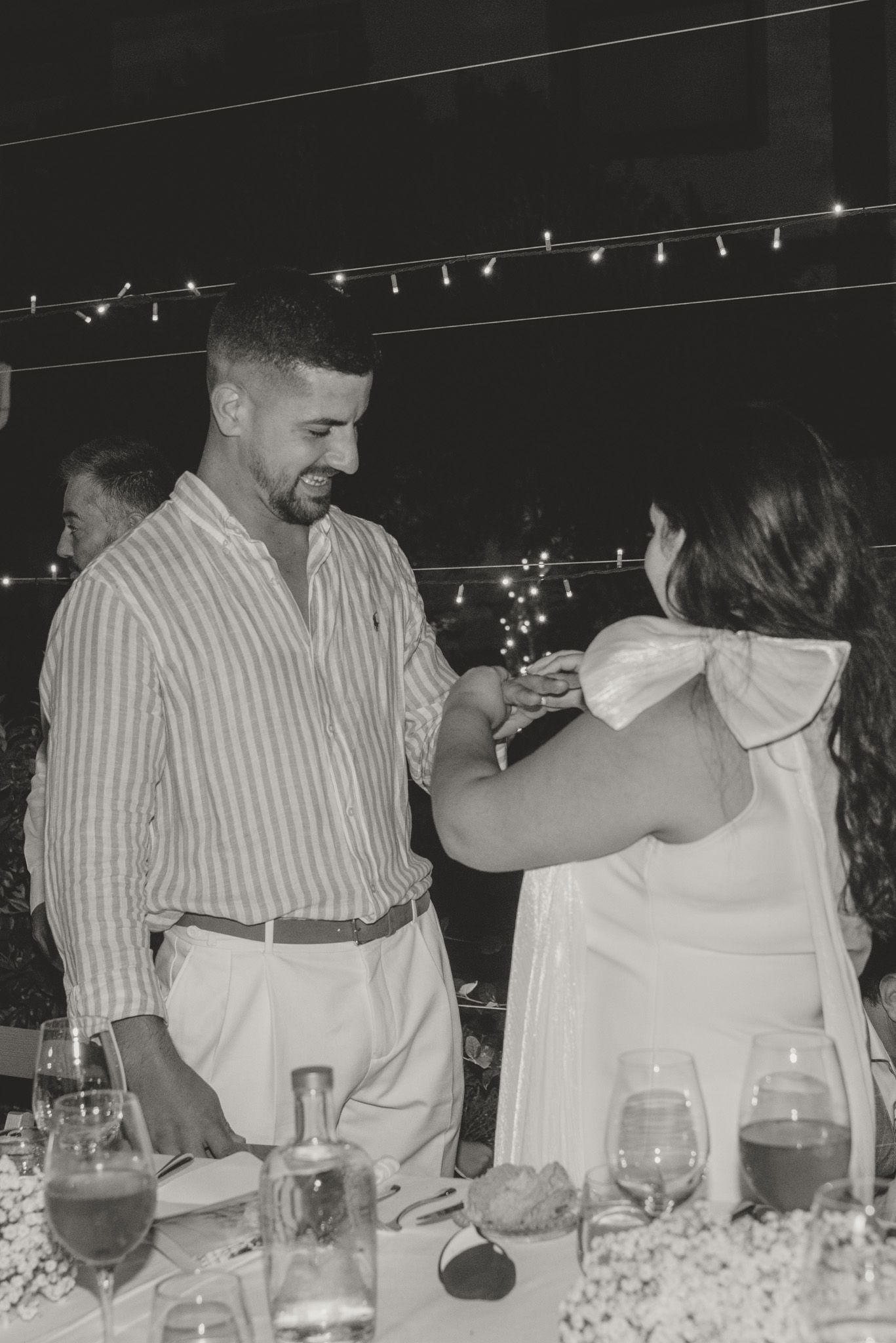 A couple sharing a playful moment during their evening celebration under string lights.