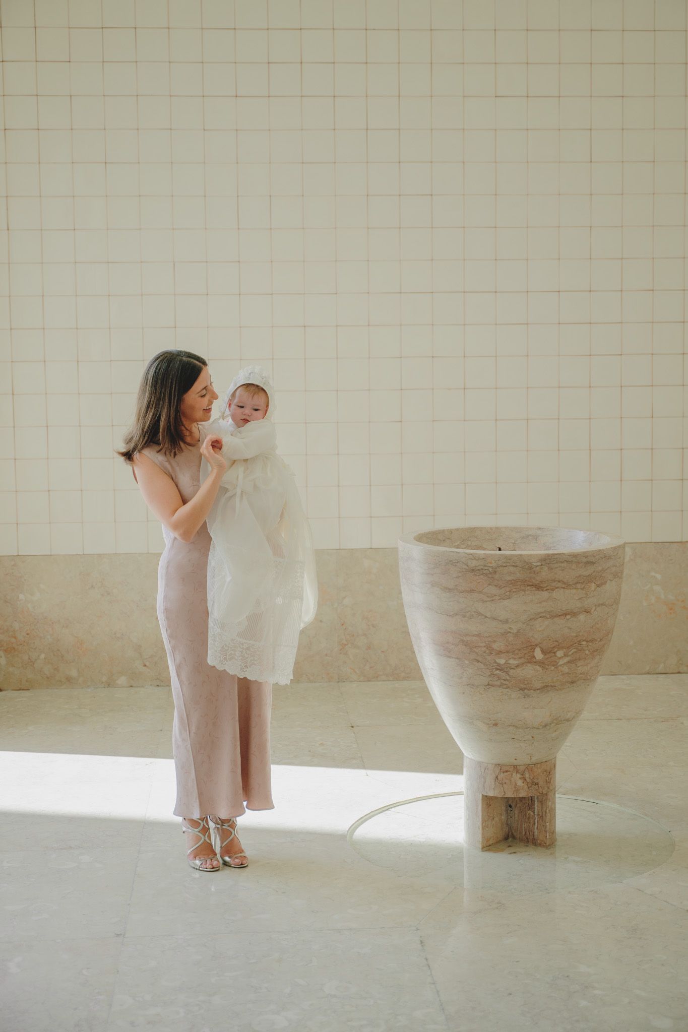 A baptismal ceremony takes place beside a stone font in a bright, minimalist space.