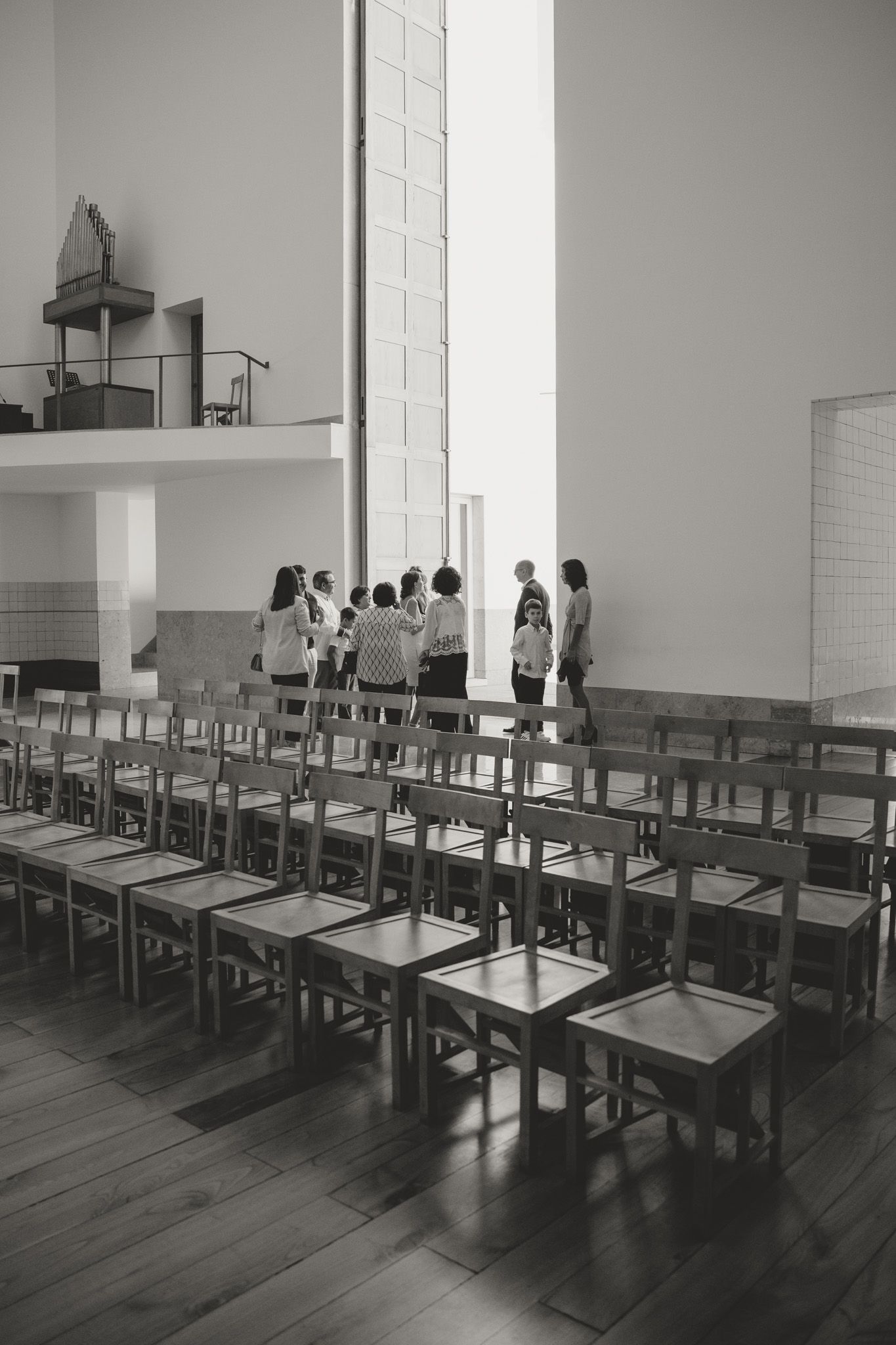 Empty classroom with wooden floors and rows of desks lit by natural light through tall windows.