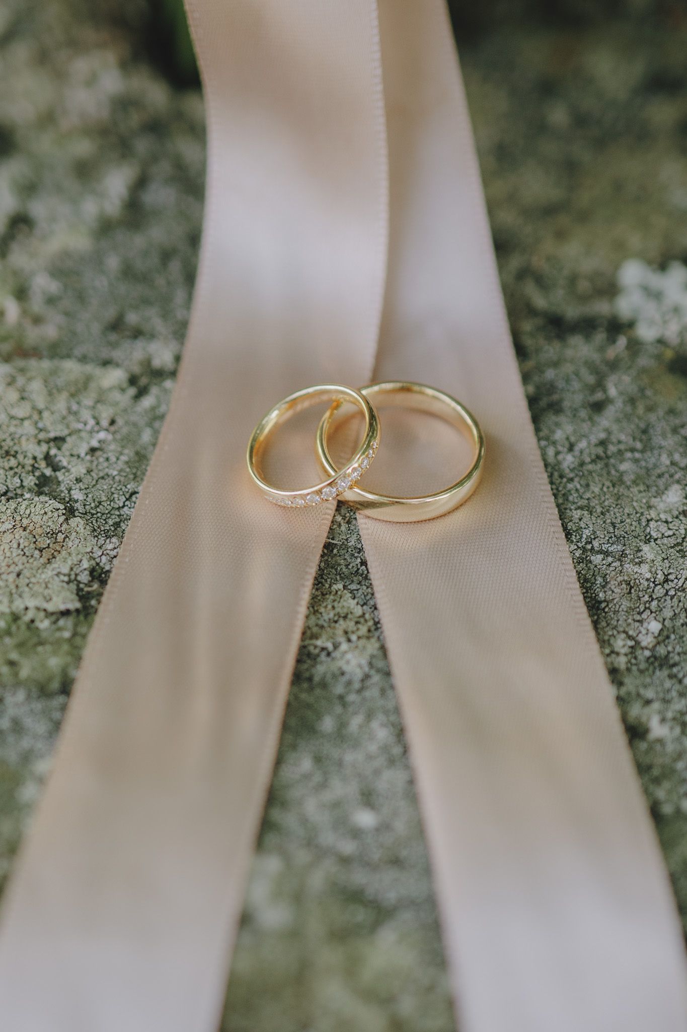 Gold wedding rings displayed on white ribbon against a textured stone background.