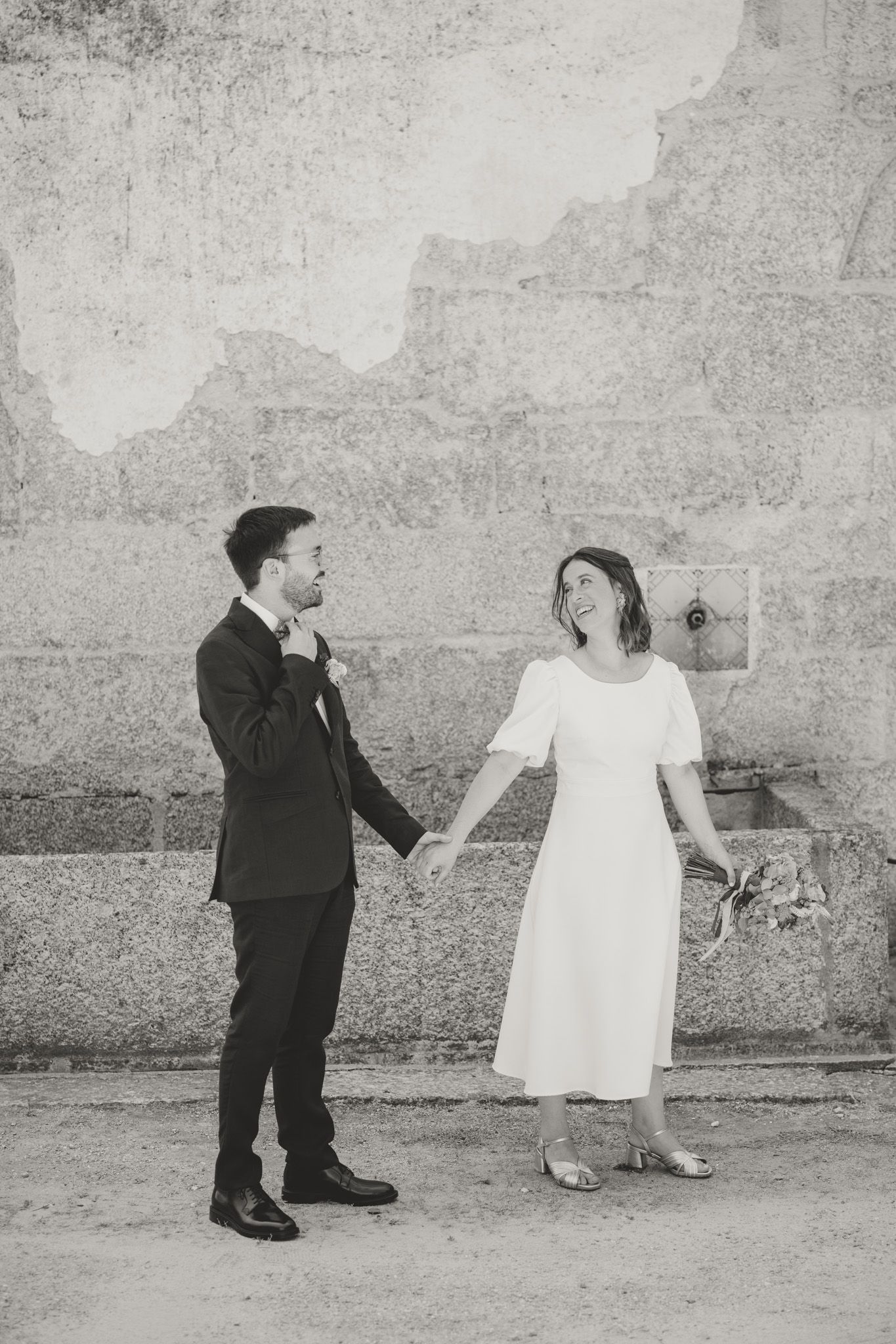 Playful black and white wedding photo against textured wall.