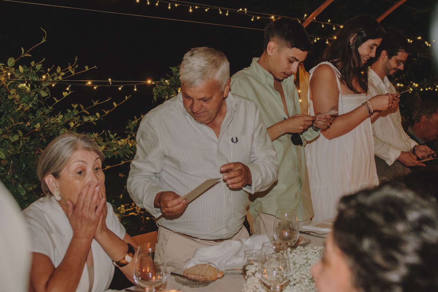 Wedding party members seated at a table during a nighttime outdoor celebration.