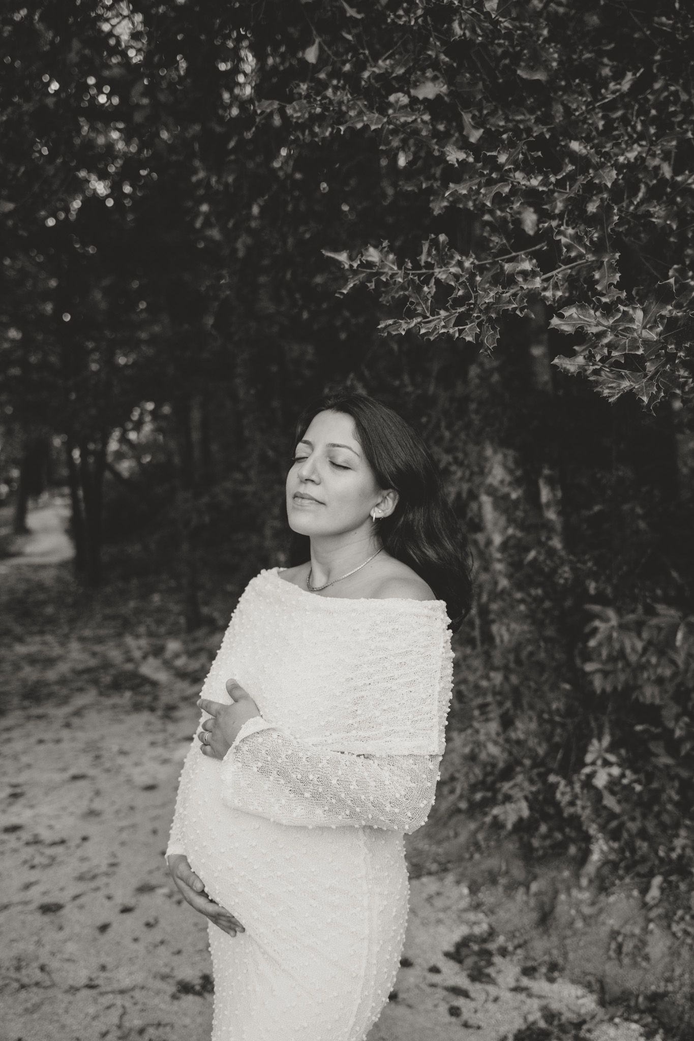 Black and white maternity portrait in a serene woodland setting.