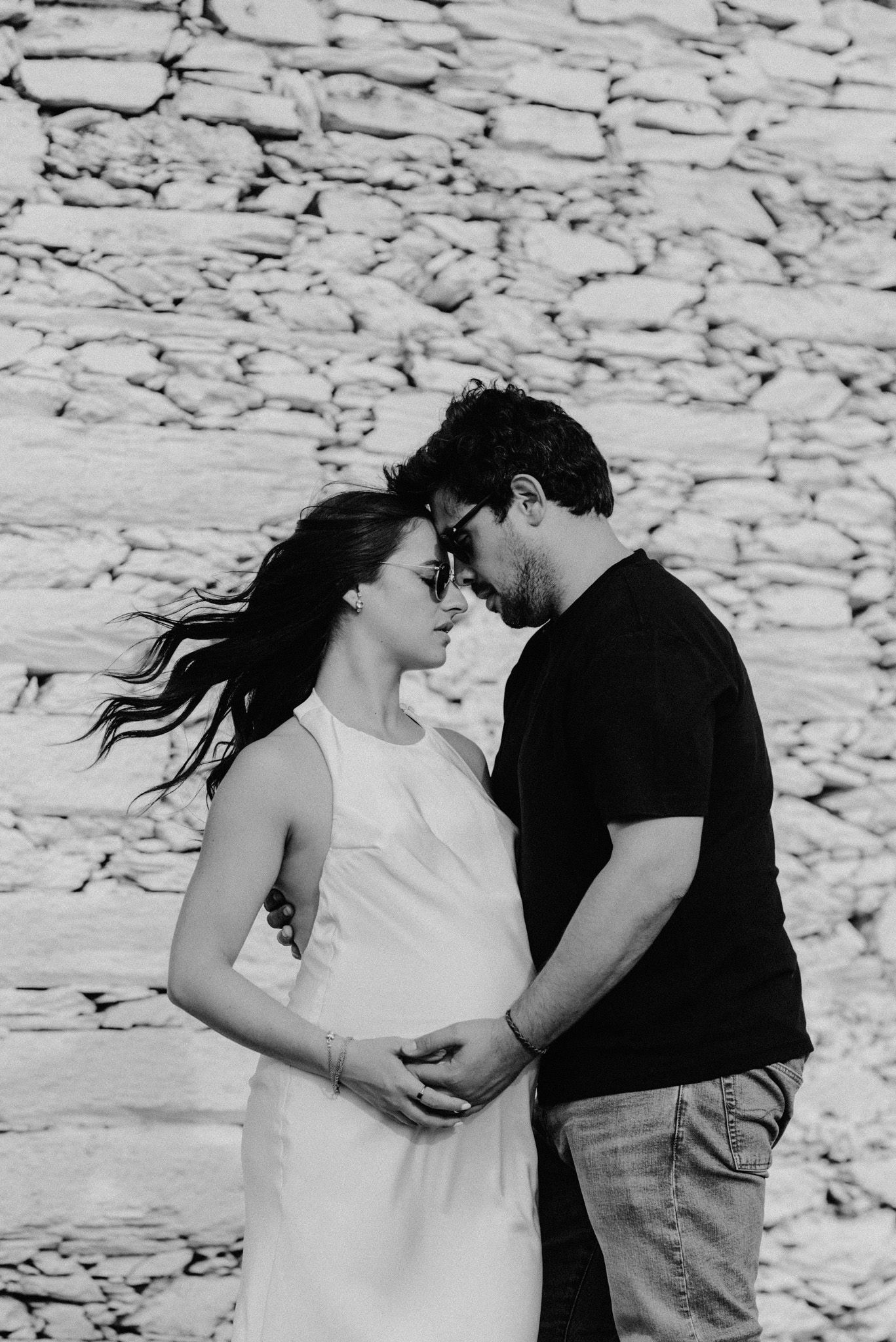 A romantic black and white photo series showing a couple embracing against a stone wall backdrop.