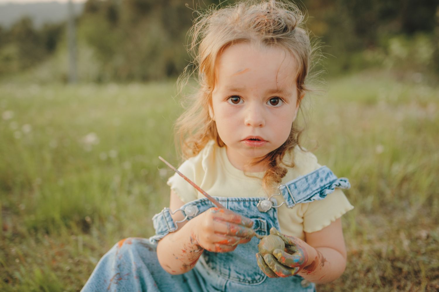 A child in a blue dress plays with a toy gun in a grassy outdoor setting during summer.