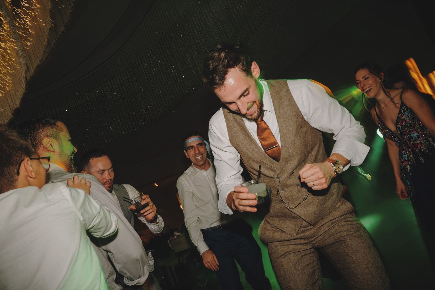 Wedding reception dance floor moments captured under green ambient lighting.