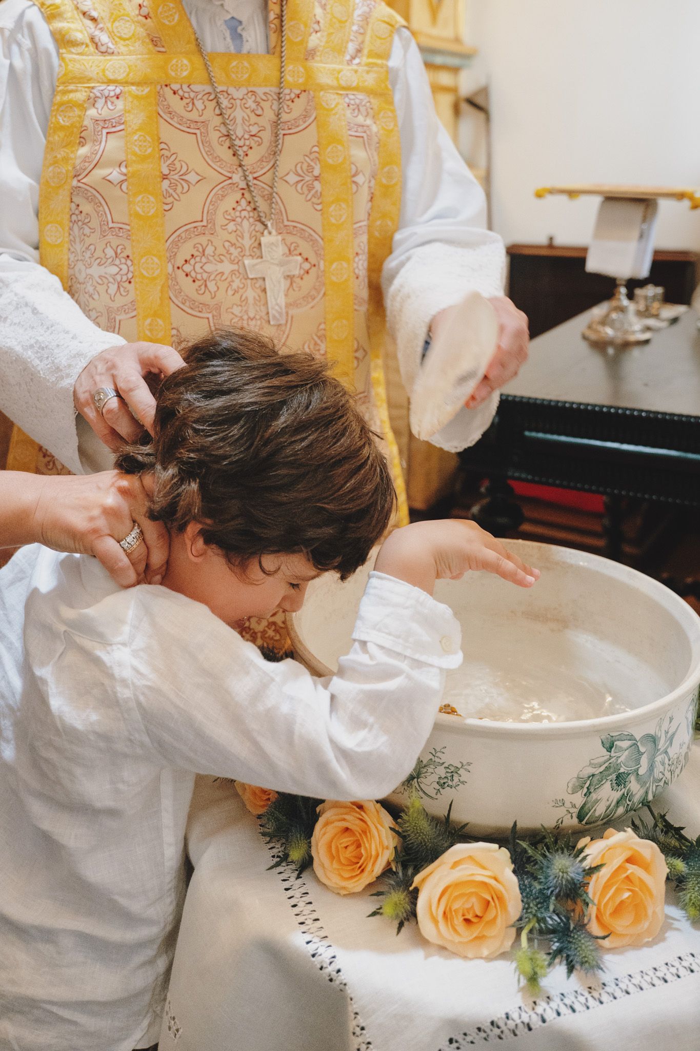Yellow-decorated baptismal font with roses during a church ceremony.