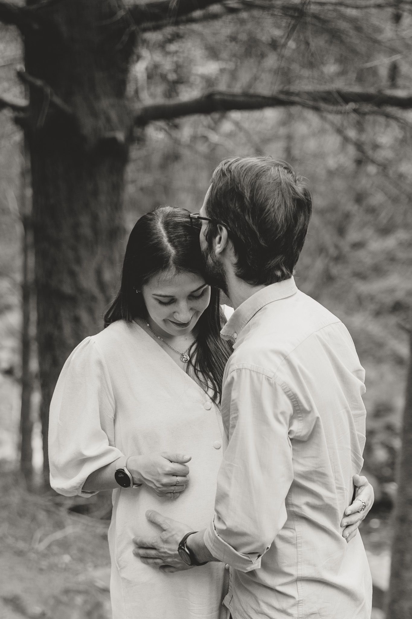 An intimate black and white portrait of a couple sharing a tender moment in the woods.