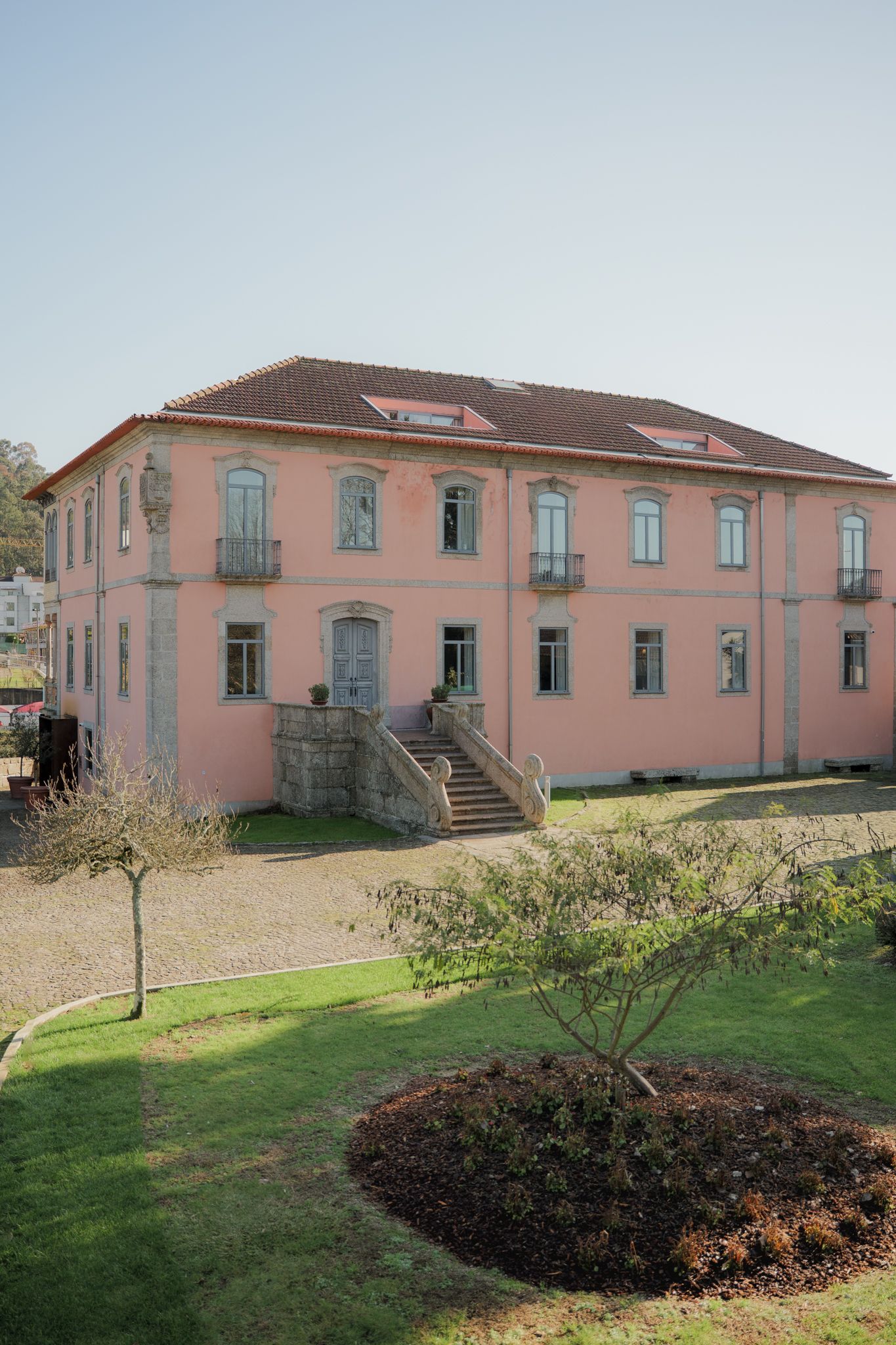 Large pink historic mansion with multiple windows and balconies set on a grassy landscape.