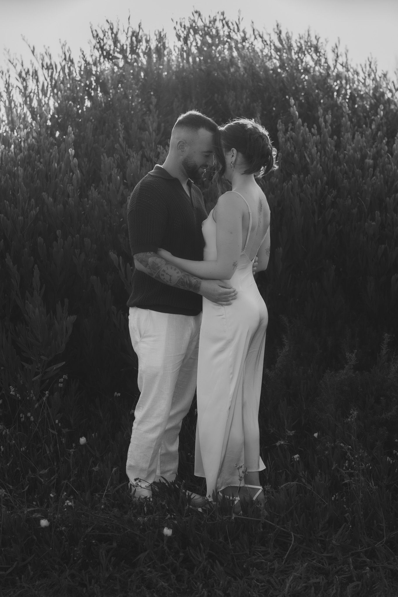Couple in white and black outfits sharing intimate moments against a natural backdrop.
