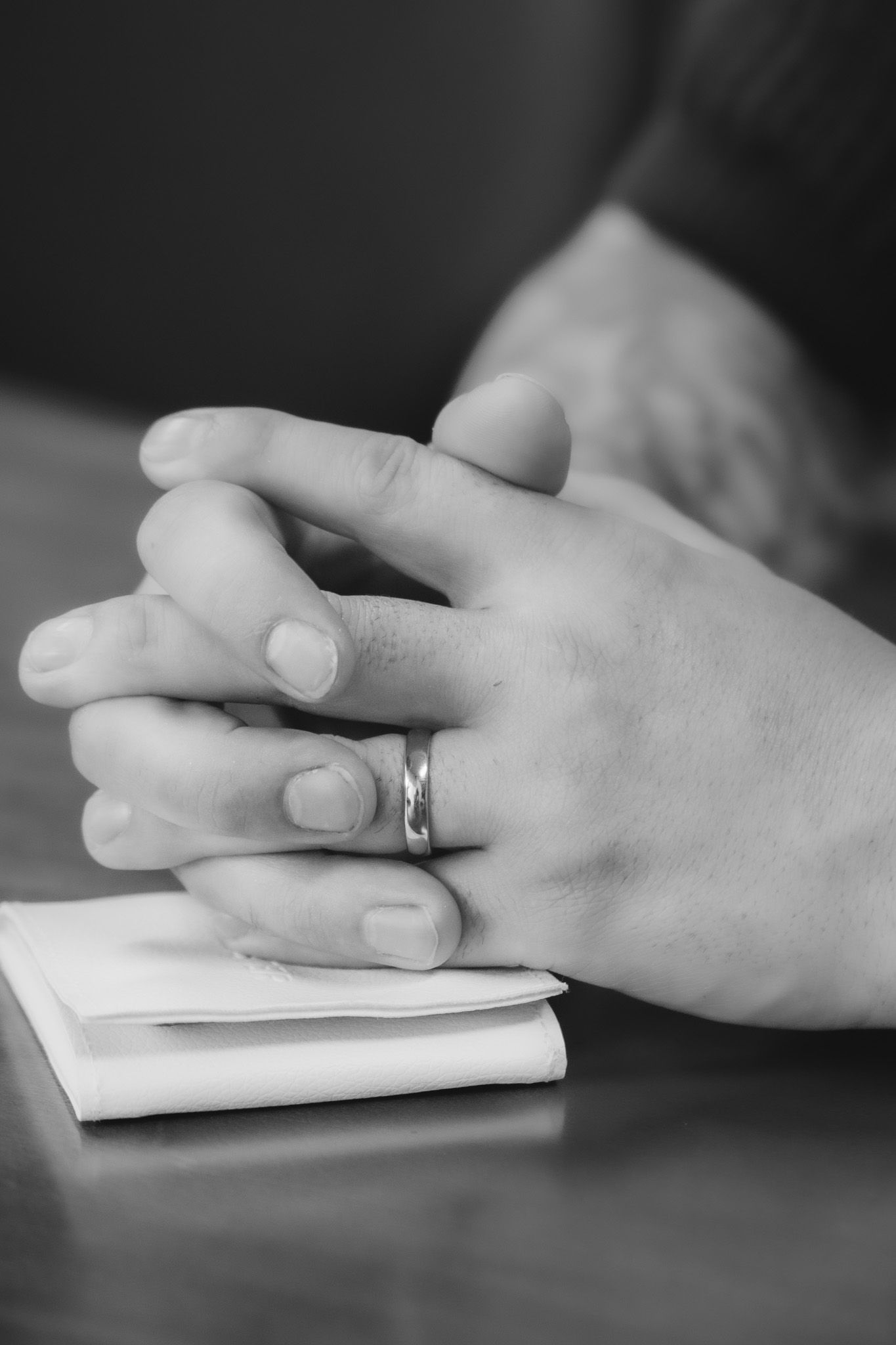 Black and white detail shot of hands with wedding ring resting on paper.