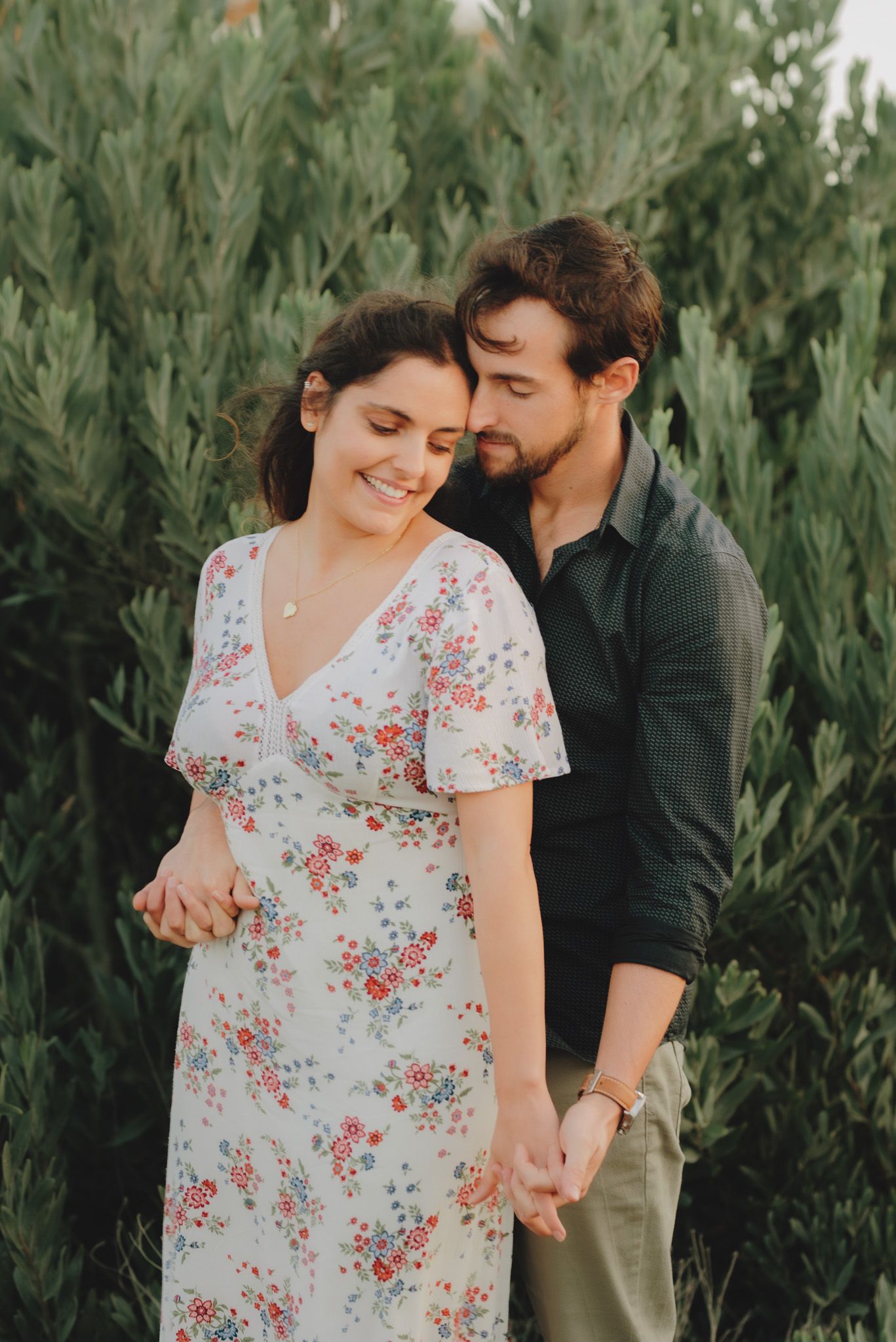 Romantic couple in a garden setting with lush greenery and floral dress details.