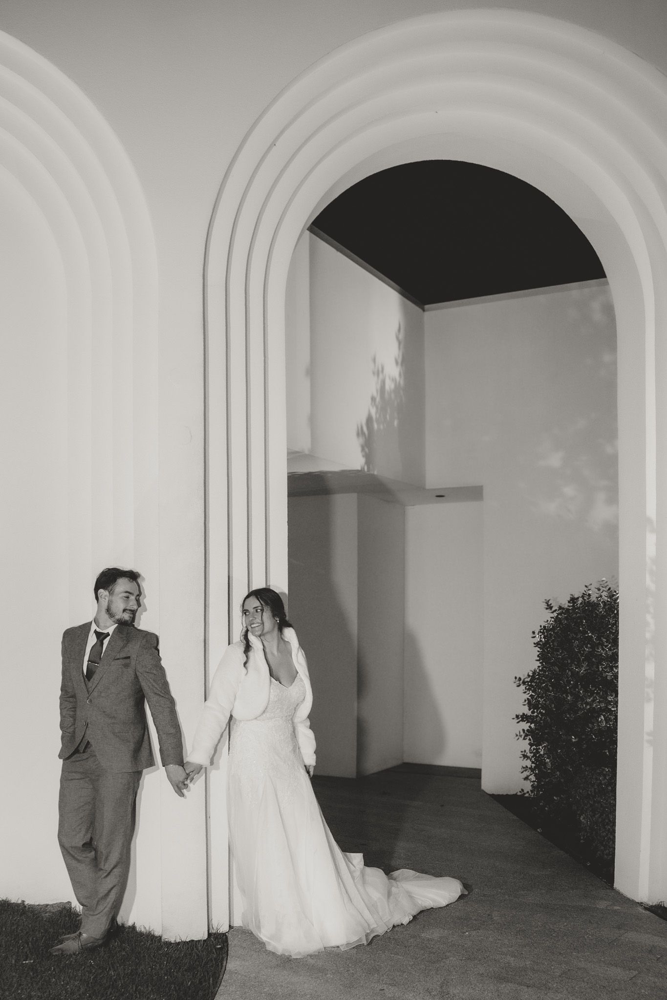 Elegant wedding couple posing in front of white arched architecture.