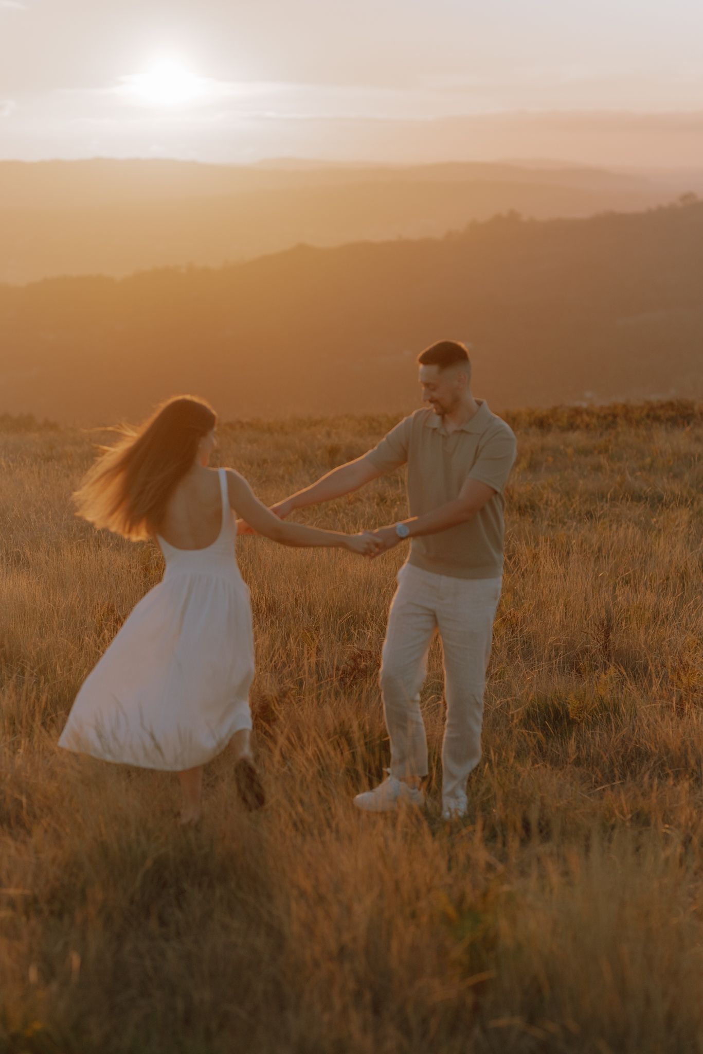 A couple dances through tall grass in a field at golden hour.