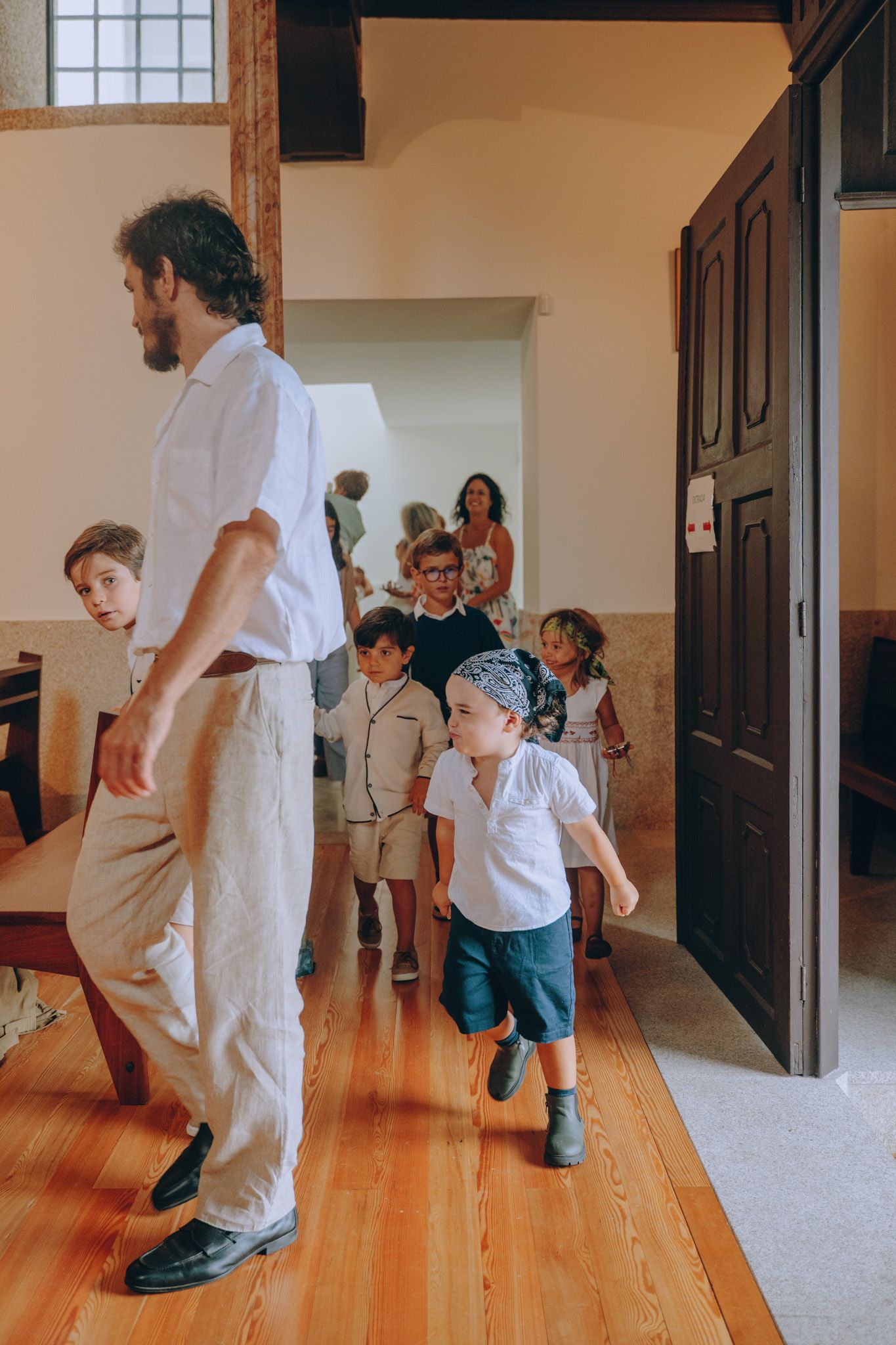 People walking and playing in a hallway with wooden floors and white walls.