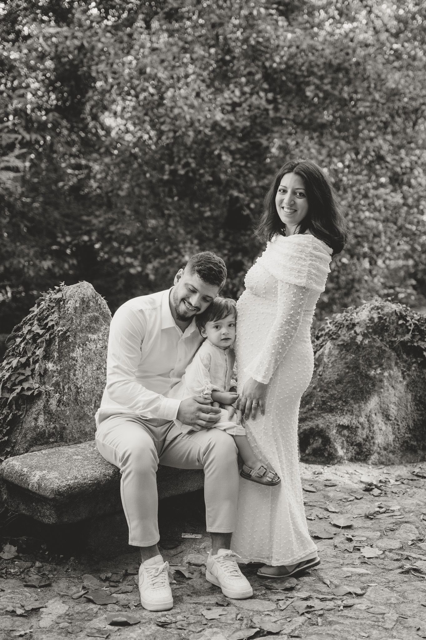 A family wearing white sits together on stone steps in a natural outdoor setting.