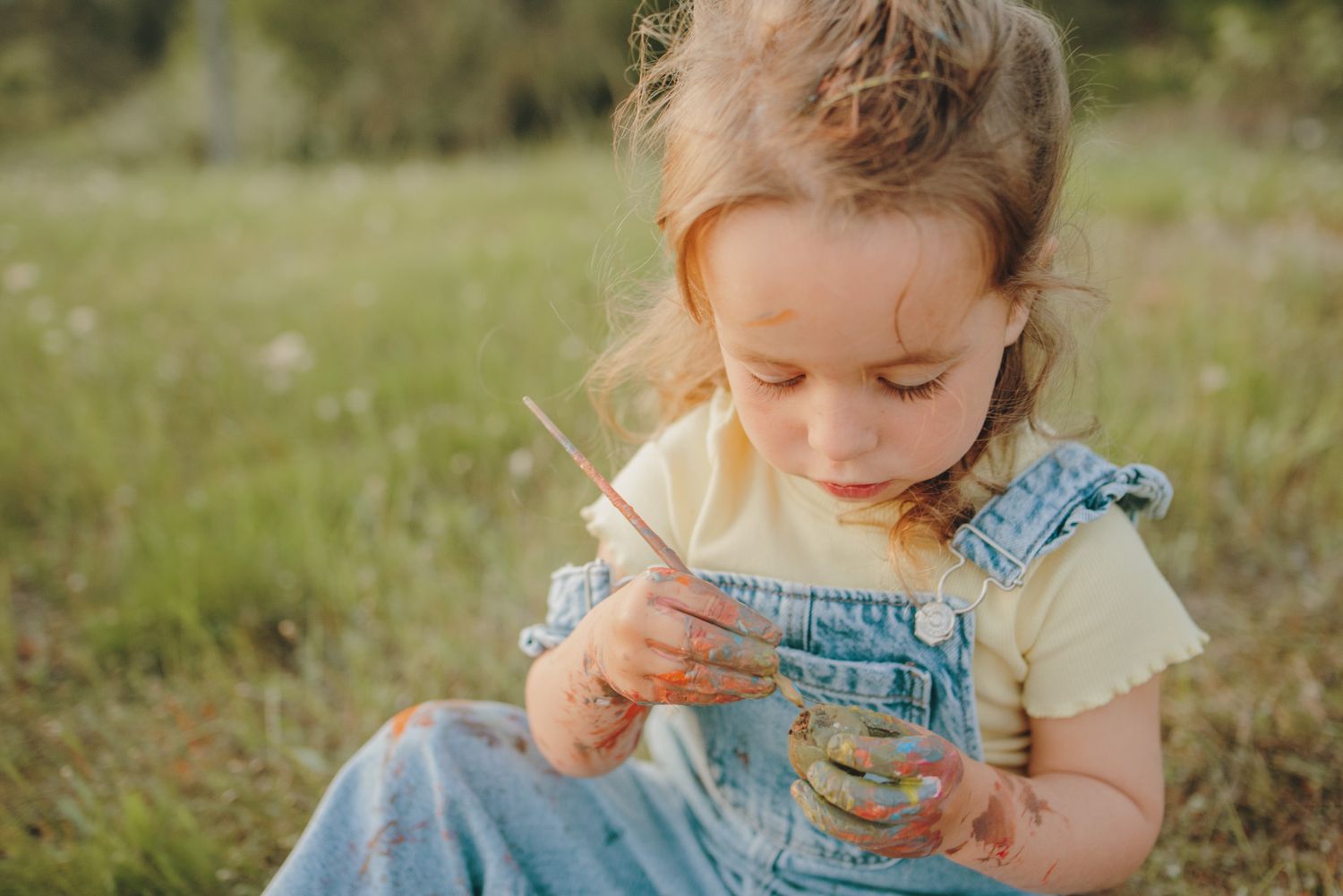 Young reader in denim overalls explores a book while sitting in nature.