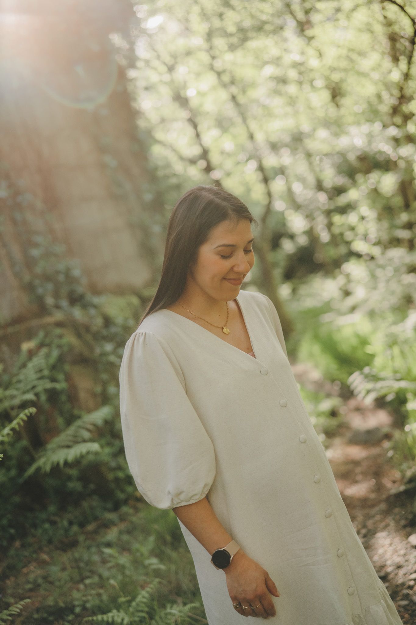 A woman in a white button-down dress stands among blooming spring trees.
